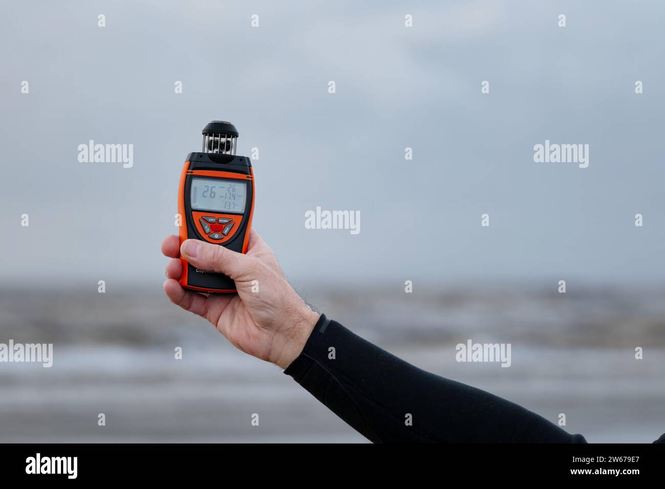 UK. A man standing on a beach holding a digital Infurider Anemometer to take a reading of the current wind speed, direction and temperature Stock Photo