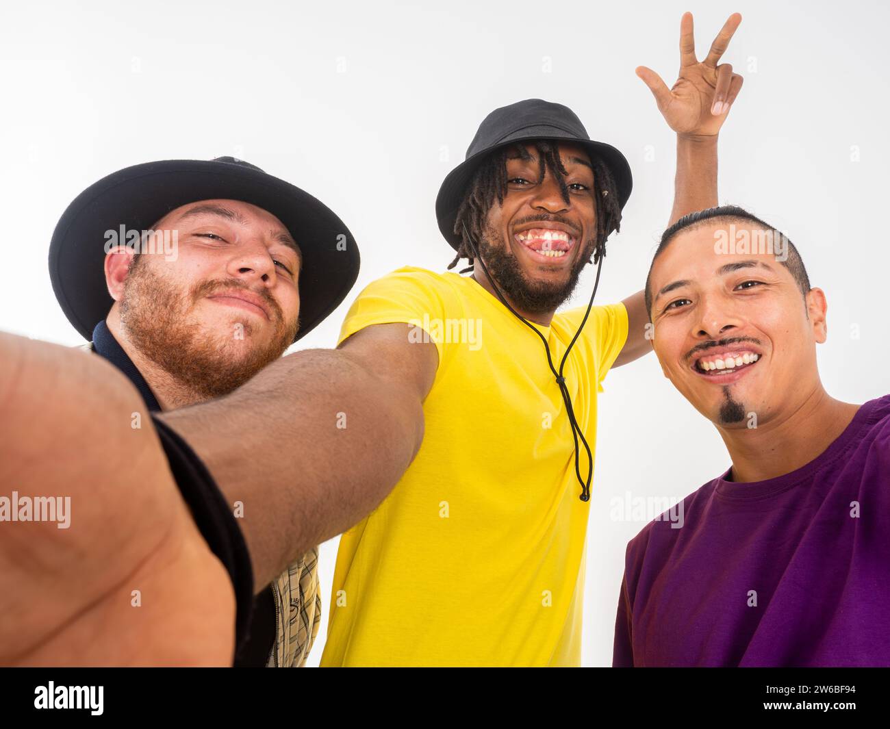 Three cheerful young men pose for a playful selfie, smiling and showing peace signs to the camera on a white background Stock Photo