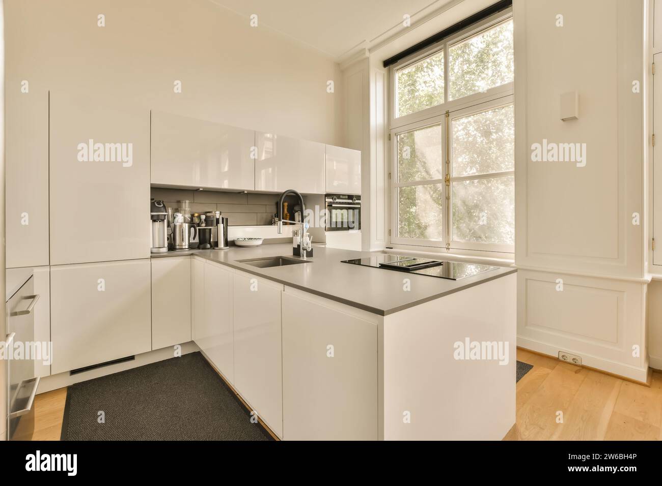Sink and induction at countertop of modern kitchen of luxurious house with large window and white cabinets Stock Photo