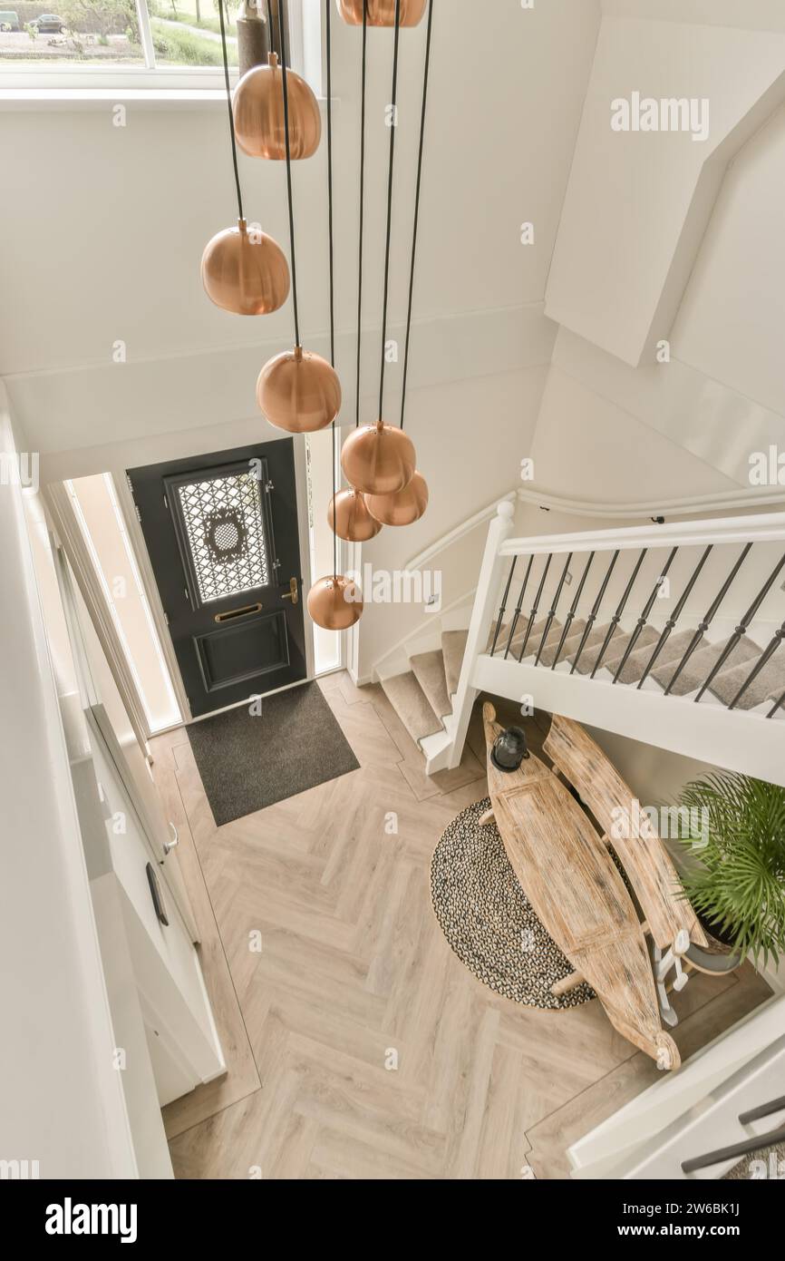 High angle of pendant lights hanging over entrance hallway with staircase and wooden bench in villa Stock Photo
