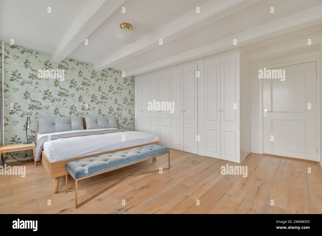 A spacious bedroom features a large bed with a stylish blue bench at