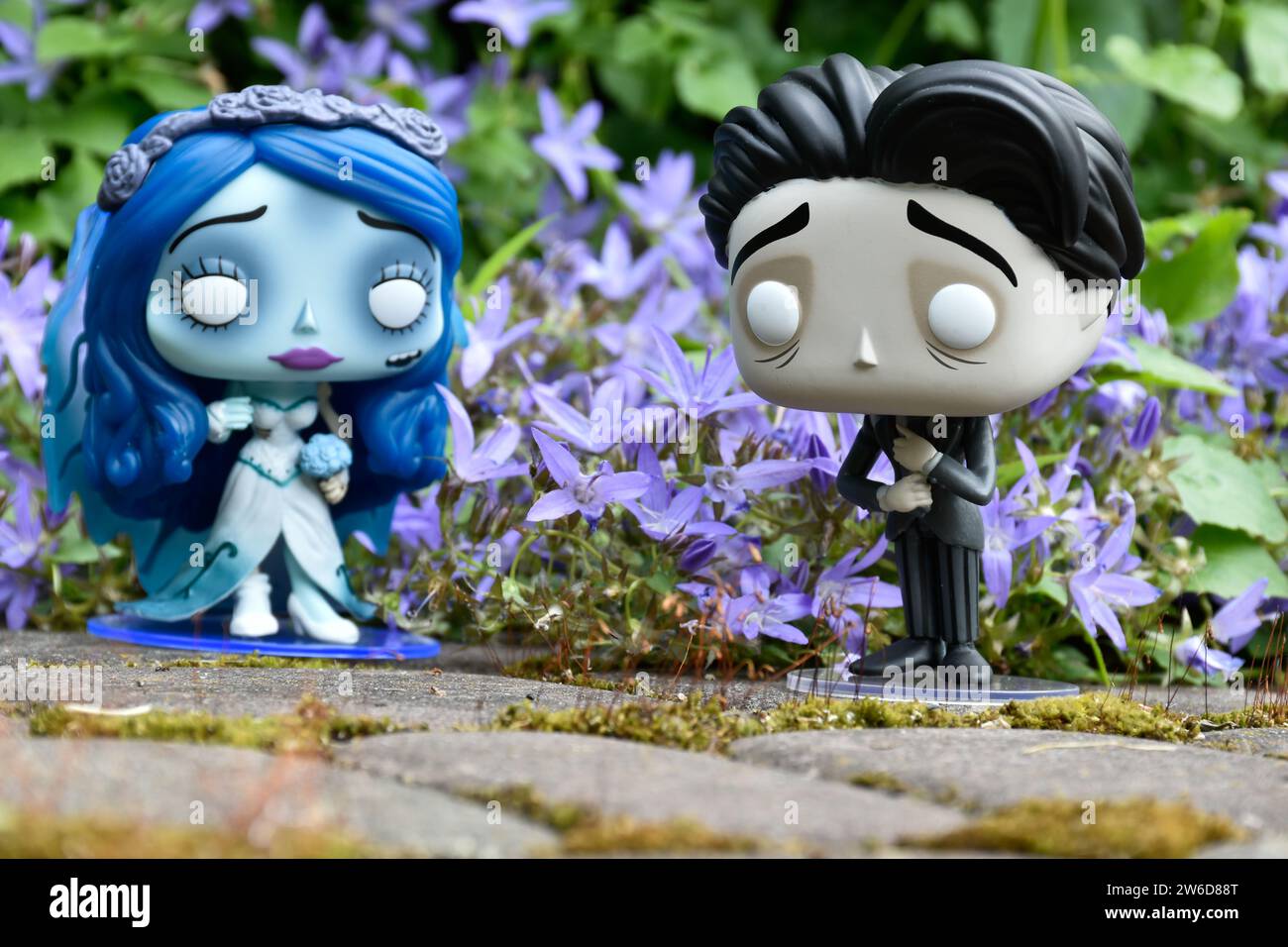 Funko Pop action figures of Emily and Victor from dark fantasy animated film Corpse Bride. Blue flowers, moss, garden, wedding, couple, romance. Stock Photo