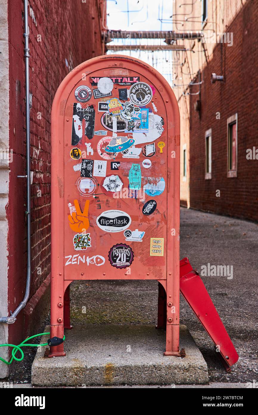 Sticker-Adorned Red Mailbox in Urban Alleyway, Eye-Level View Stock Photo
