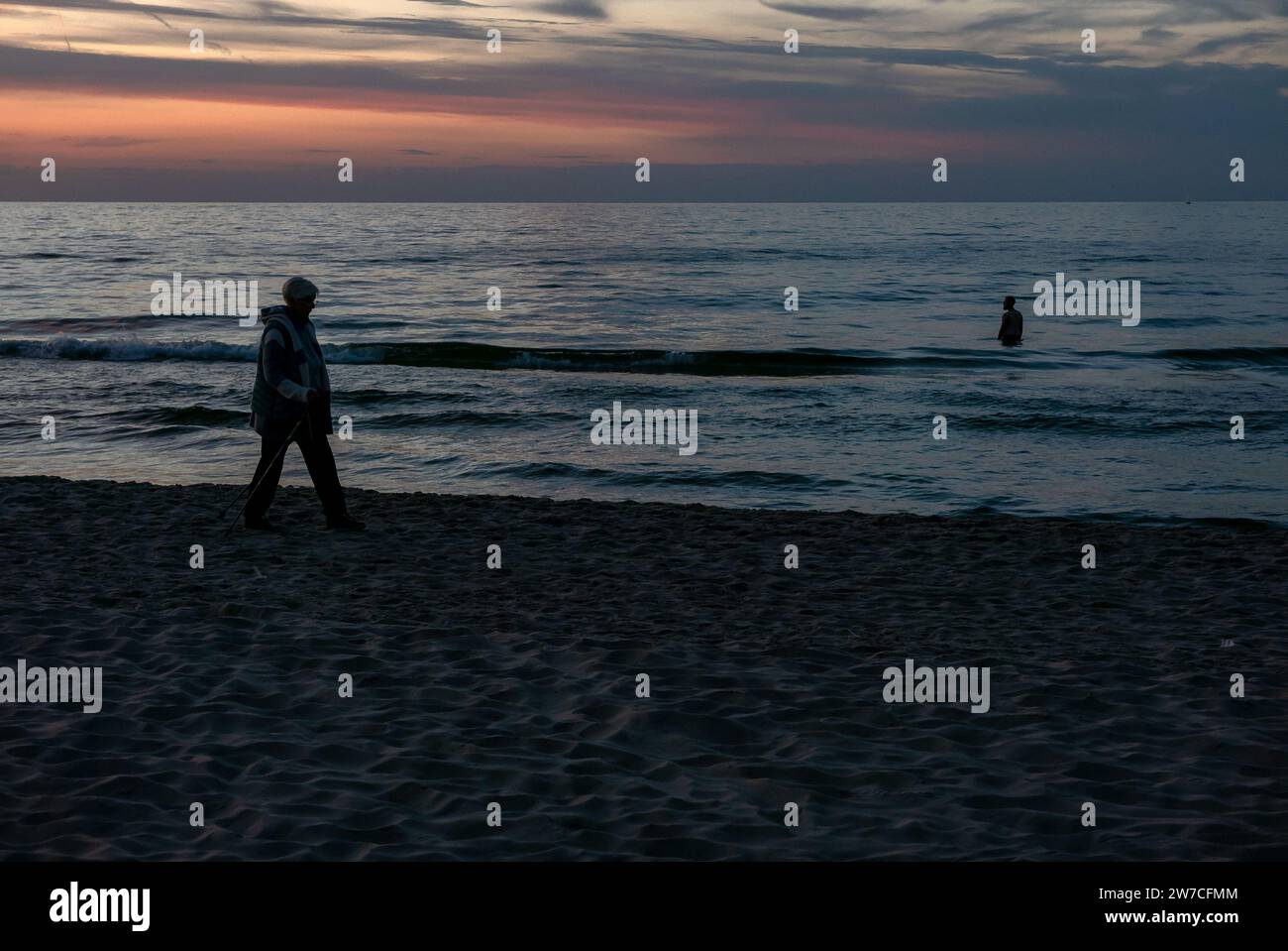 08.09.2018, Poland, Kolobrzeg, West Pomerania - Sillhouettes of holidaymakers on the Baltic Sea coast, man standing in the water at sunset. 00A180908D Stock Photo