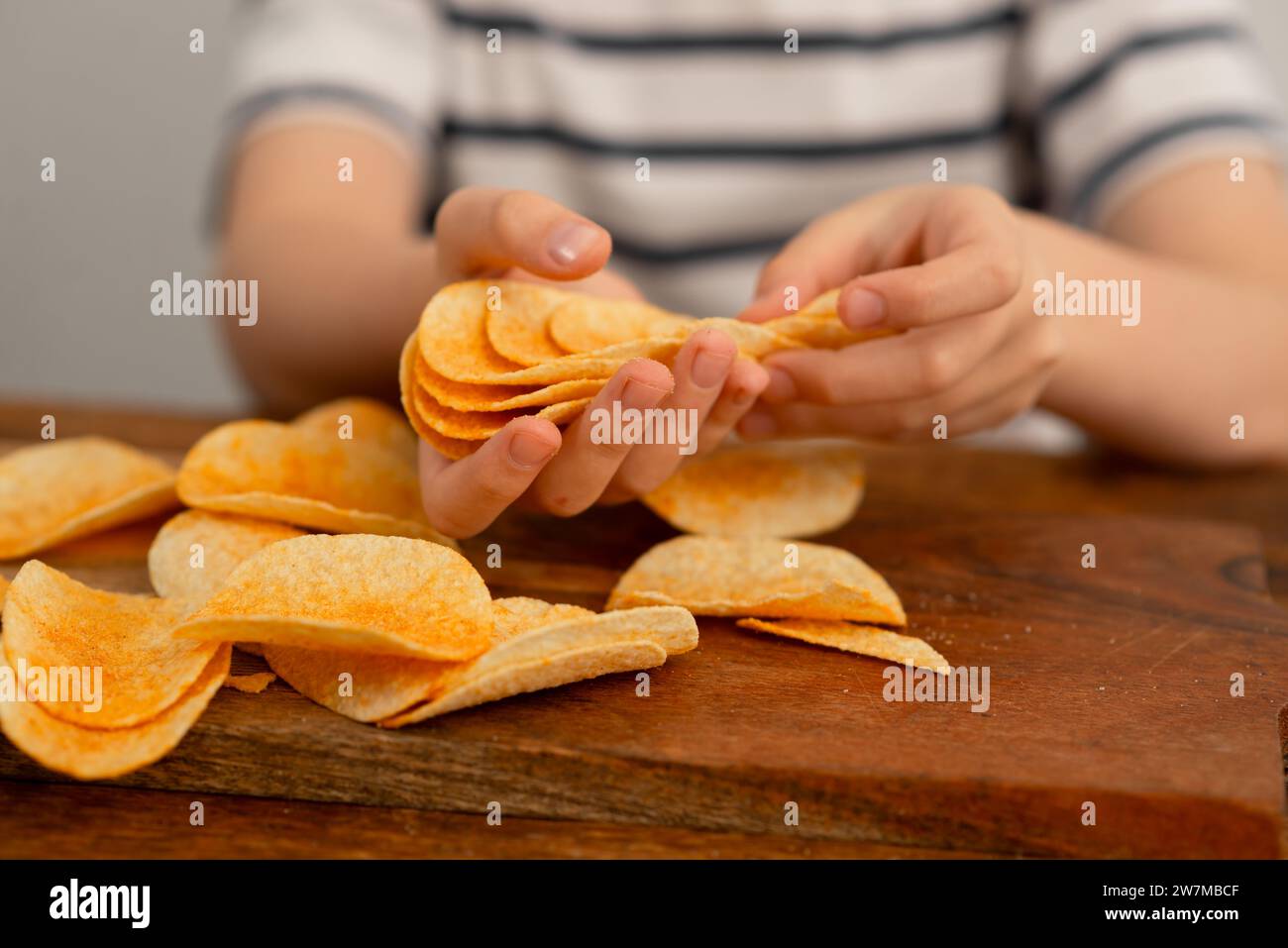 A child's hands engaging with potato chips, stacking them on a wooden table for a playful snack time. Stock Photo