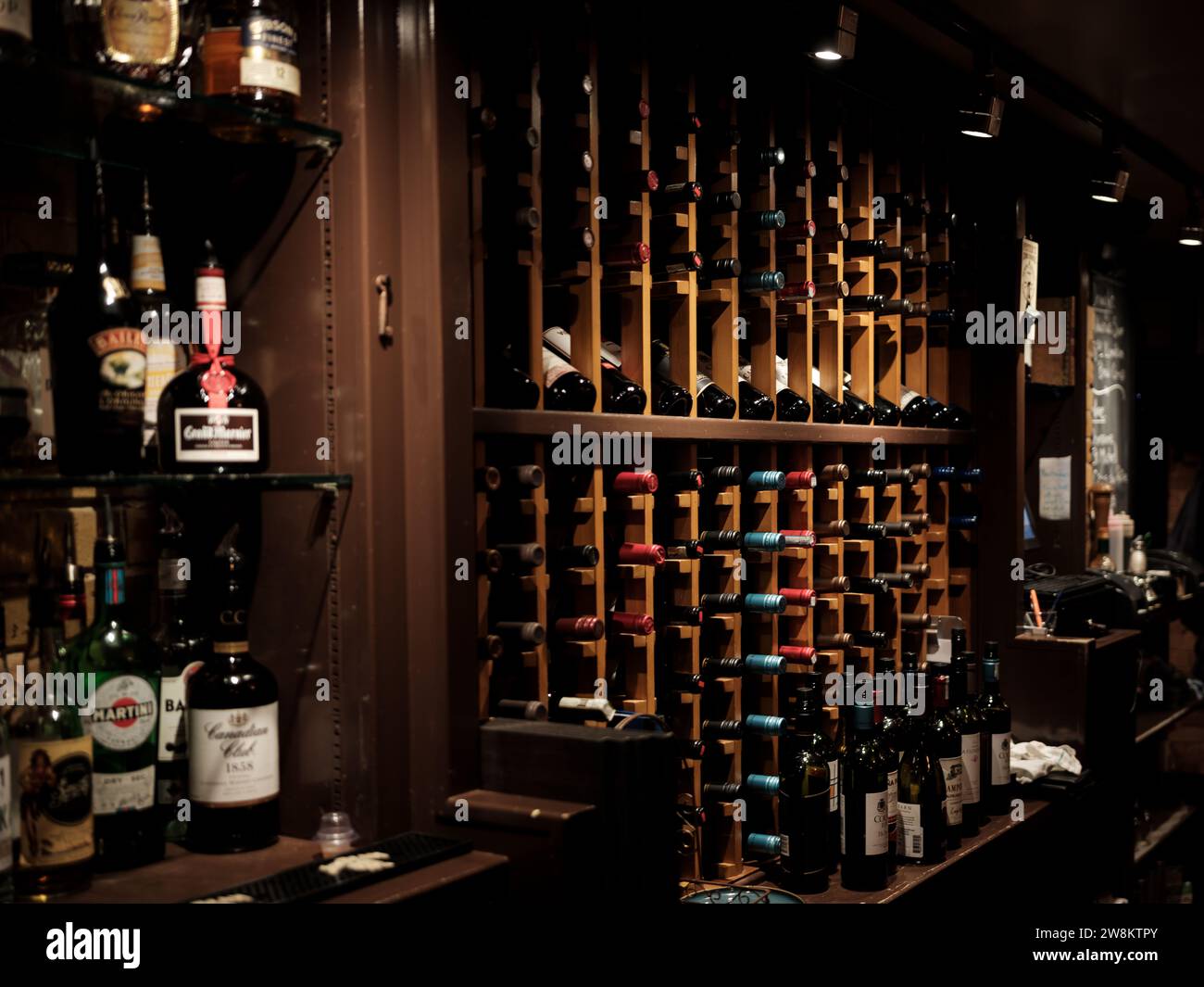 Wine and liquor bottles lined up on a bar and in a wine rack behind a