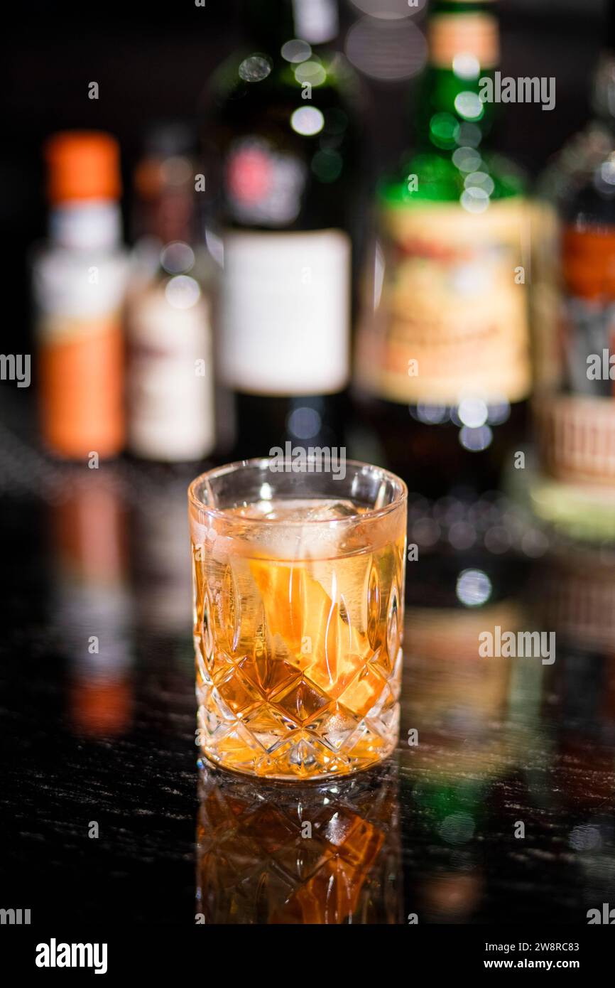 Alcohol cocktail with ice, liquor bottles in background Stock Photo