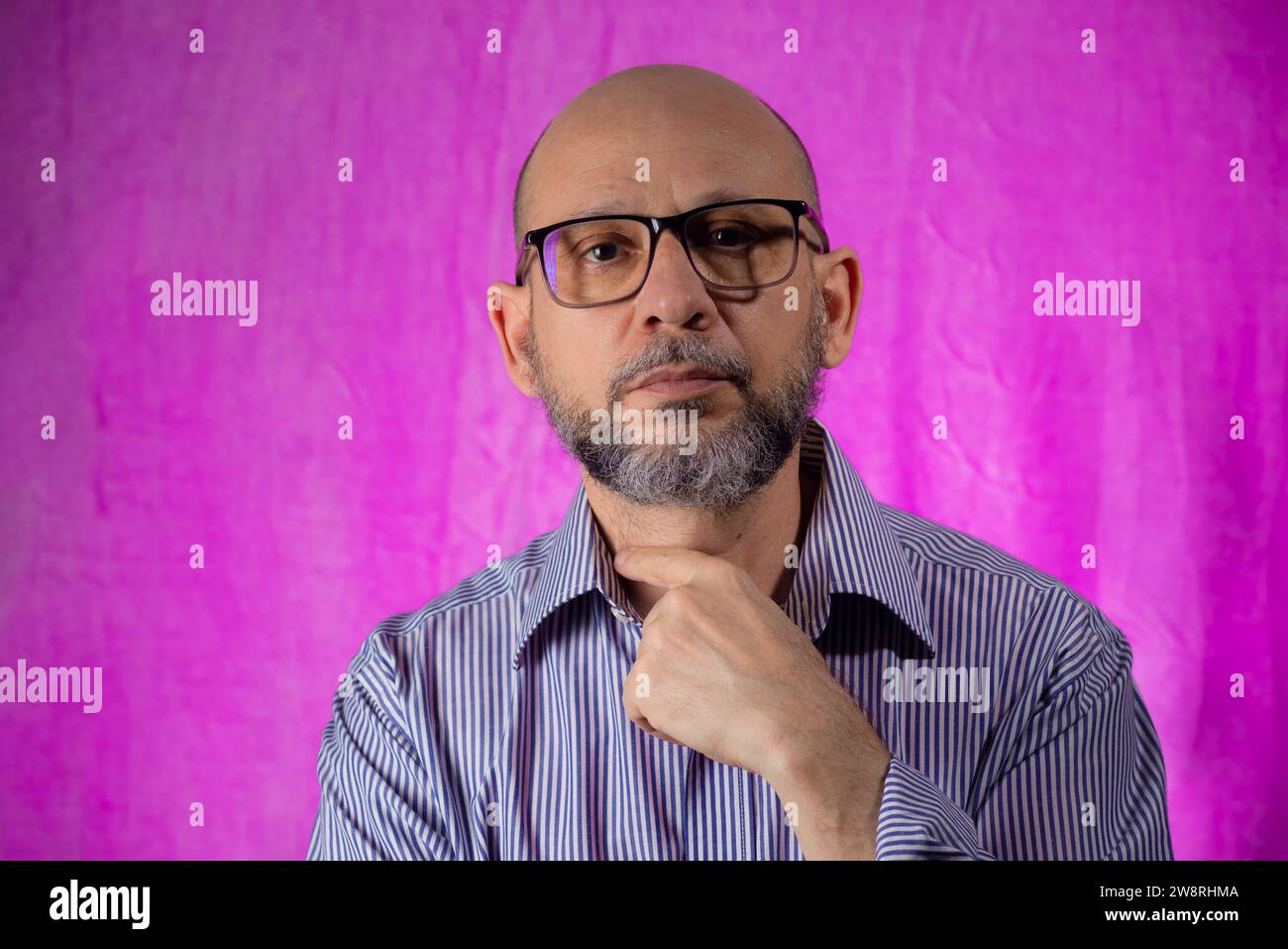 Bald, bearded man looking at camera against pink background. Stock Photo