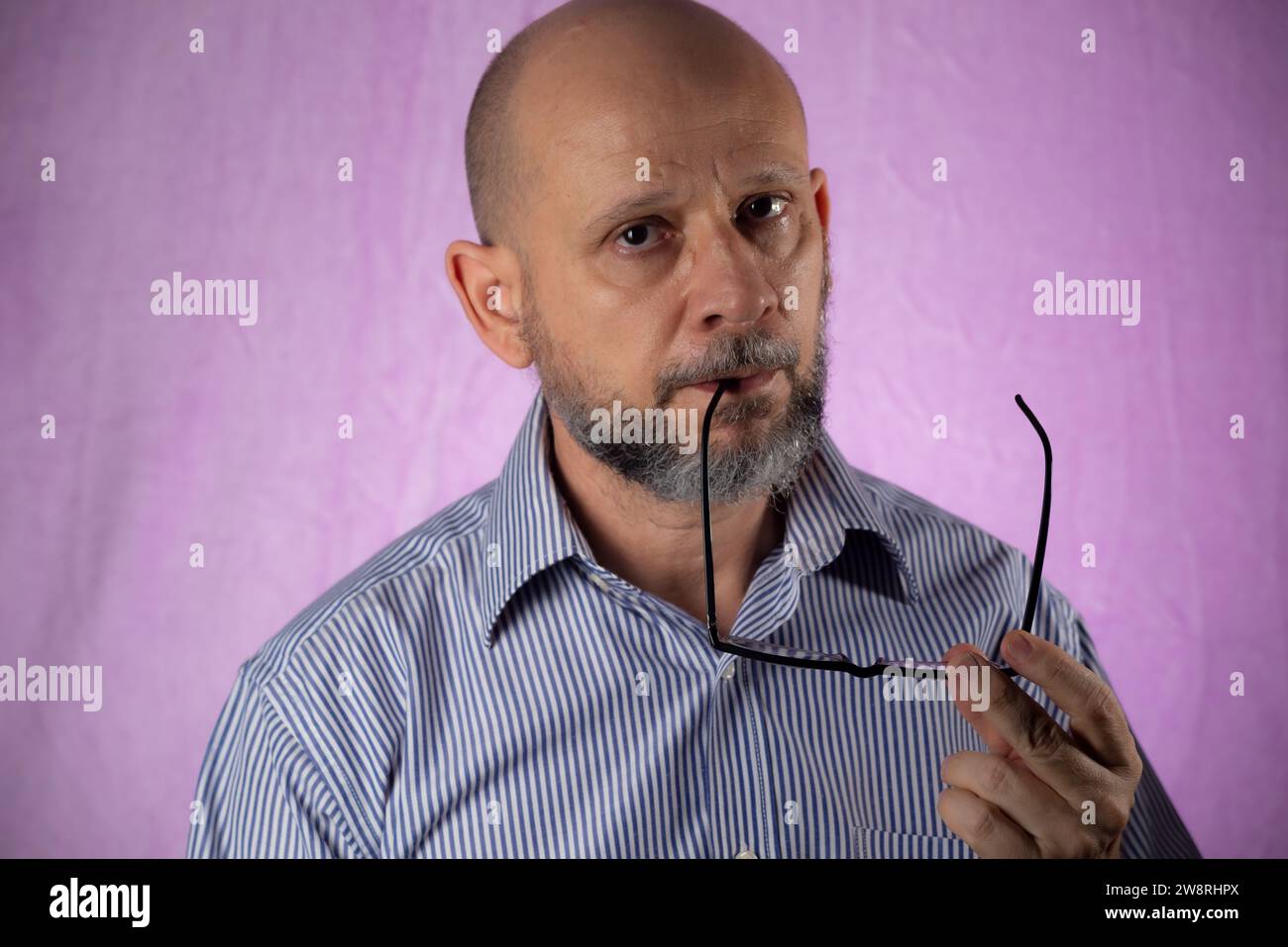 Bearded and bald man holding prescription glasses against pink background. Stock Photo