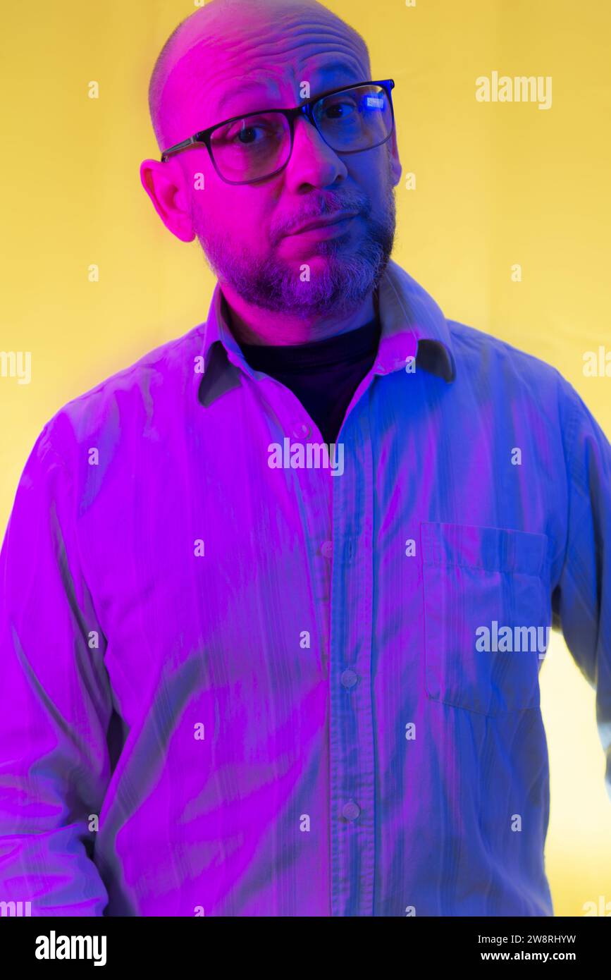 Bald, bearded man wearing prescription glasses against yellow background. Stock Photo