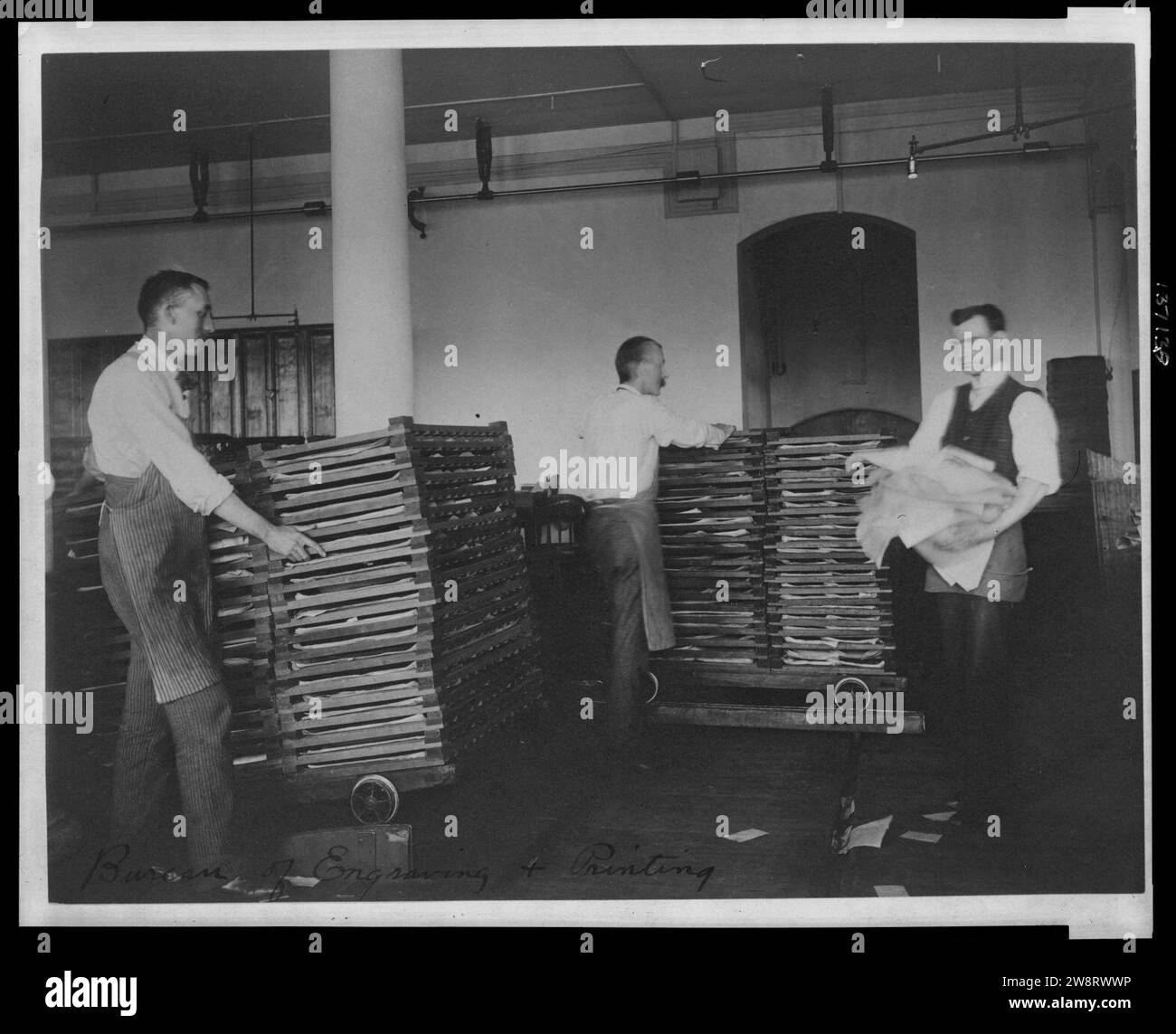 Workers moving newly printed currency into a drying box where sheets