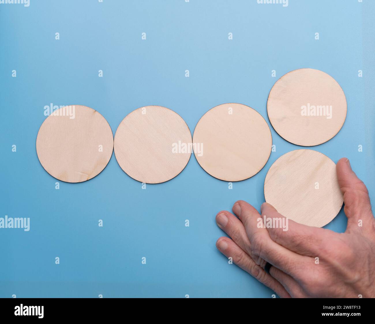Mans hand placing a wooded circle on a blue background Stock Photo Alamy