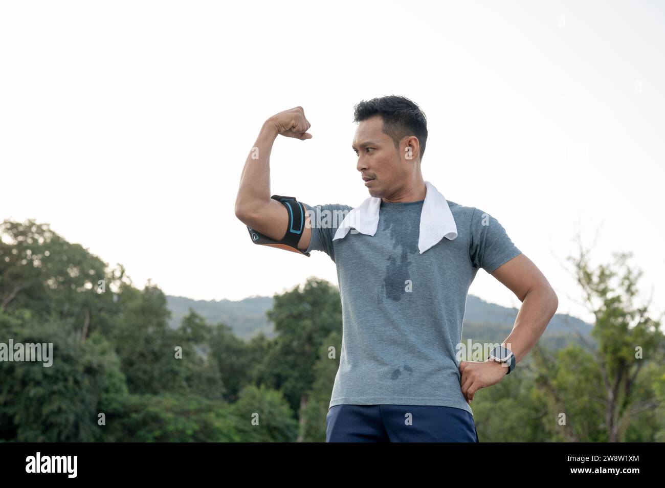 A strong Asian man in sportswear is showing his strong arm muscle, running exercise outdoors. male athlete, marathon, jogger, runner Stock Photo
