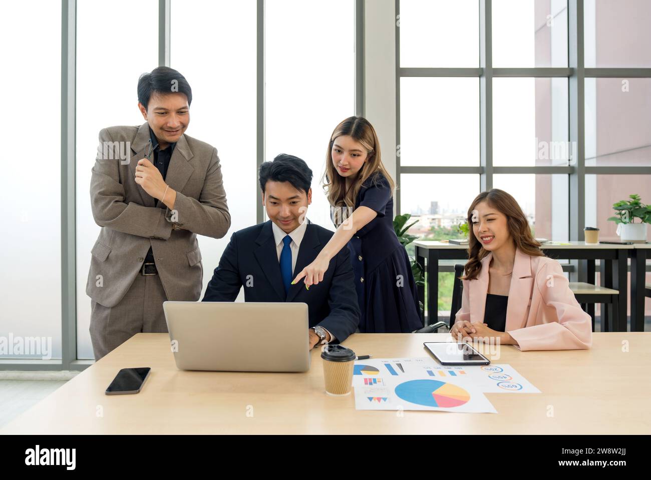 Business professionals collaborating with enthusiasm while examining data on a laptop in a contemporary office setting. Stock Photo