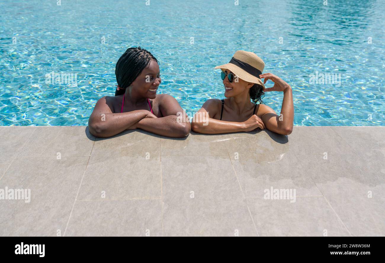 Two women are relaxing together on the edge of a swimming pool ...