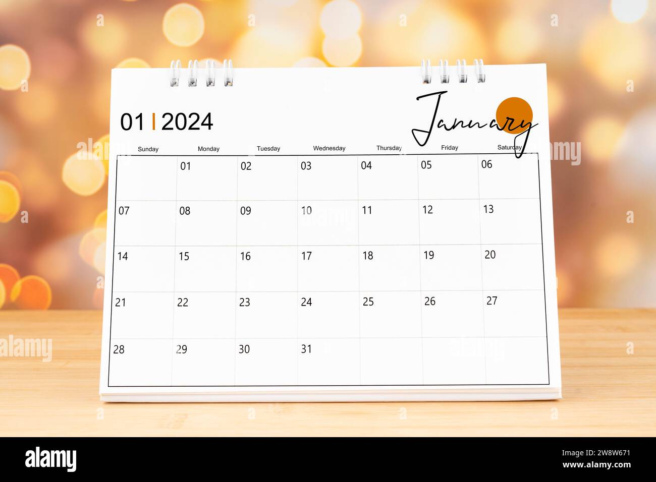 January 2024 desk calendar on wooden table with gold light bokeh