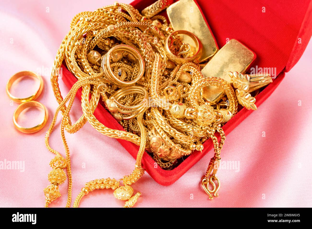 Many gold necklaces and gold bars in red box on velvet cloth background