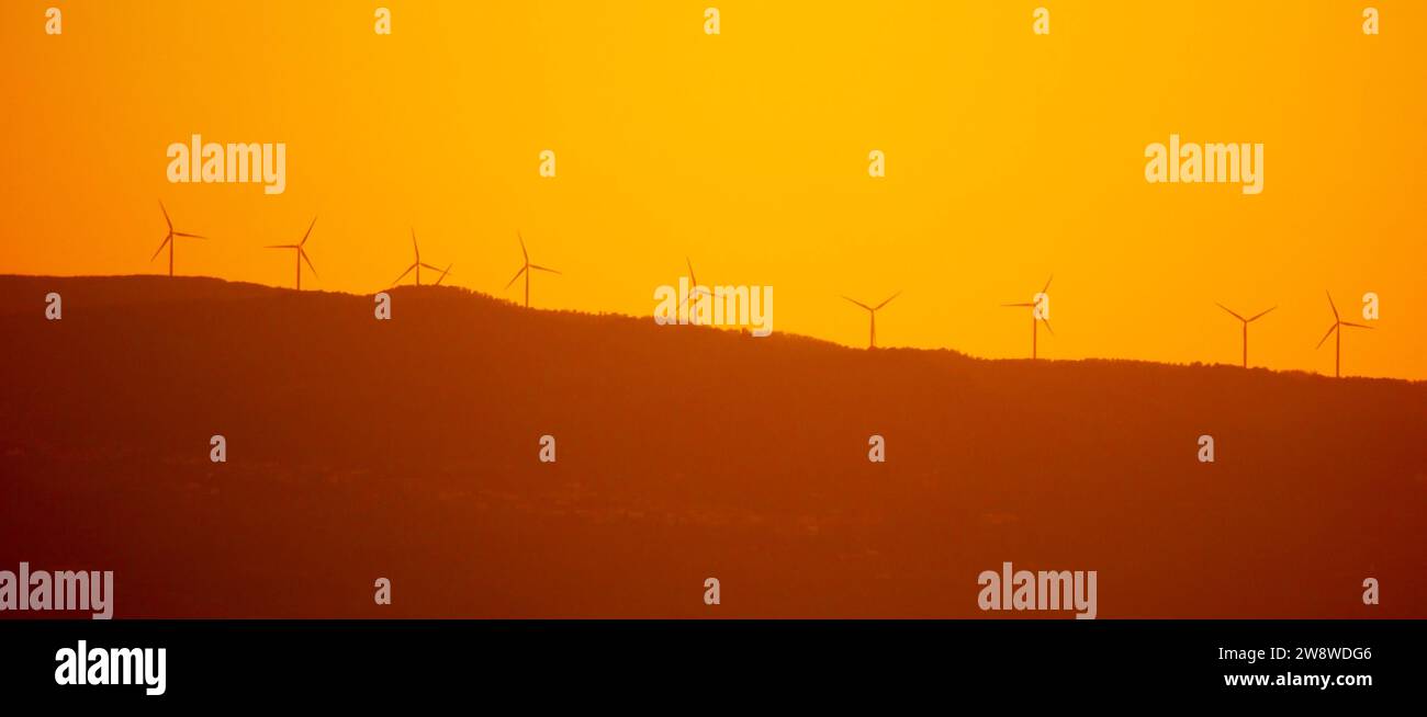 Silhouettes of wind power plant turbines on the ridge at sunset time ...