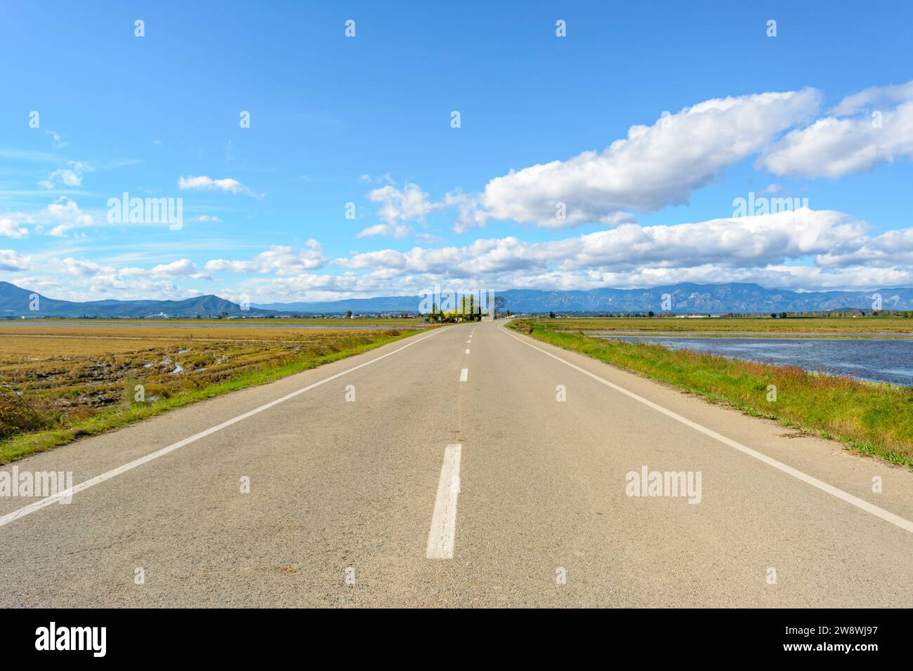 A straight road leading towards mountains under a bright blue sky Stock ...