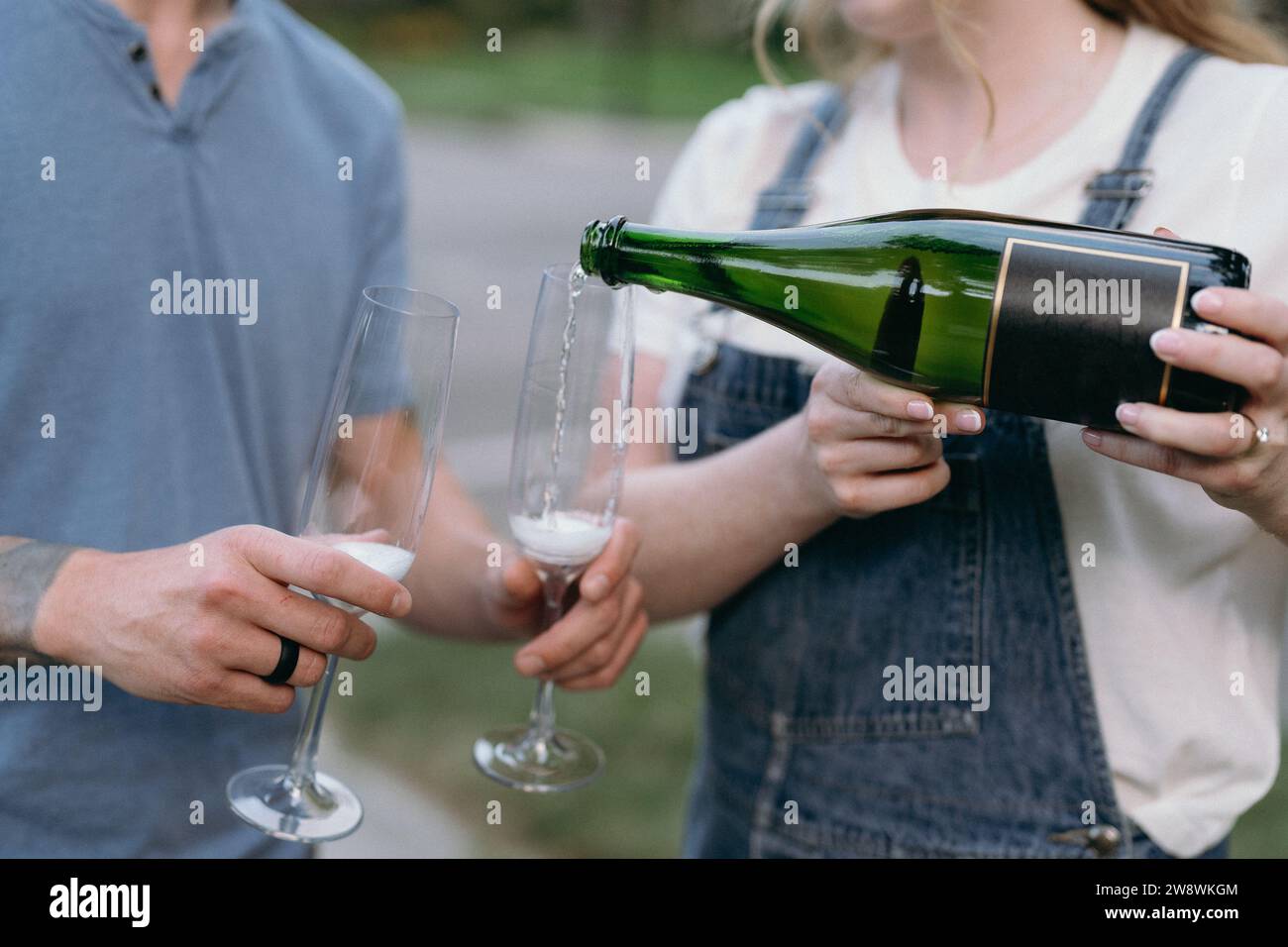 Engaged coupleâ€™s hands pouring champagne into flutes Stock Photo