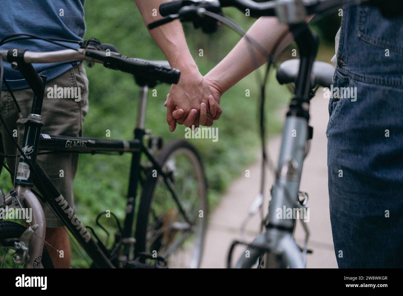 Couple on a date holding hands while walking their bicycles Stock Photo