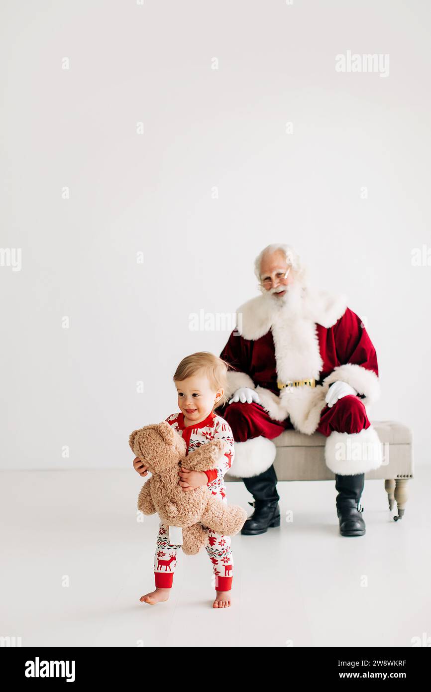 Toddler boy with teddy bear running away from Santa Claus Stock Photo