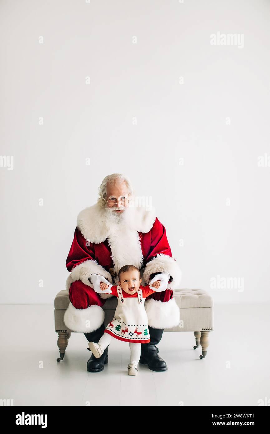 Santa Claus helping a baby girl stand up with a clean white backdrop Stock Photo