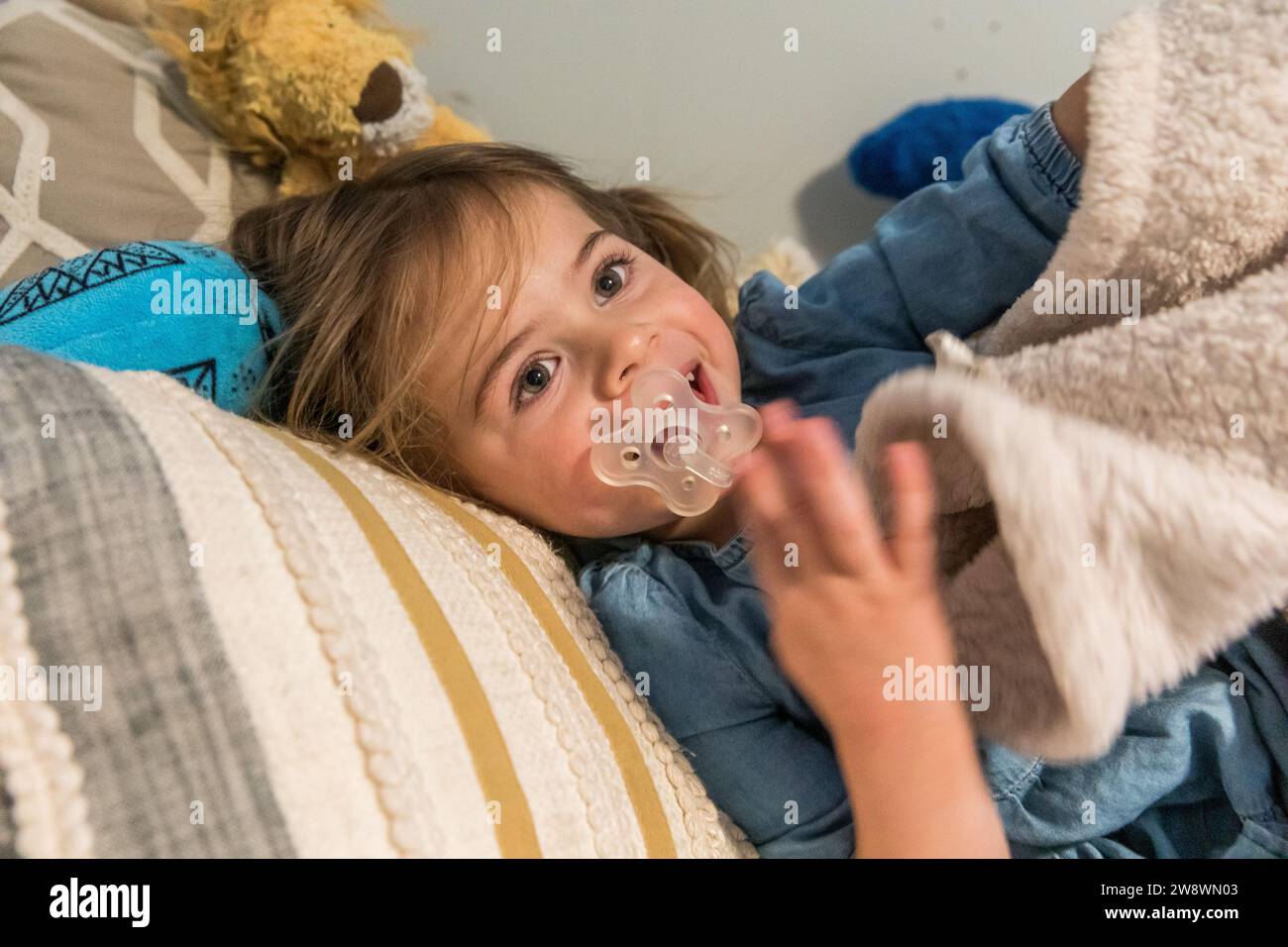 Toddler girl sucking on pacifier in bed with blanket Stock Photo Alamy