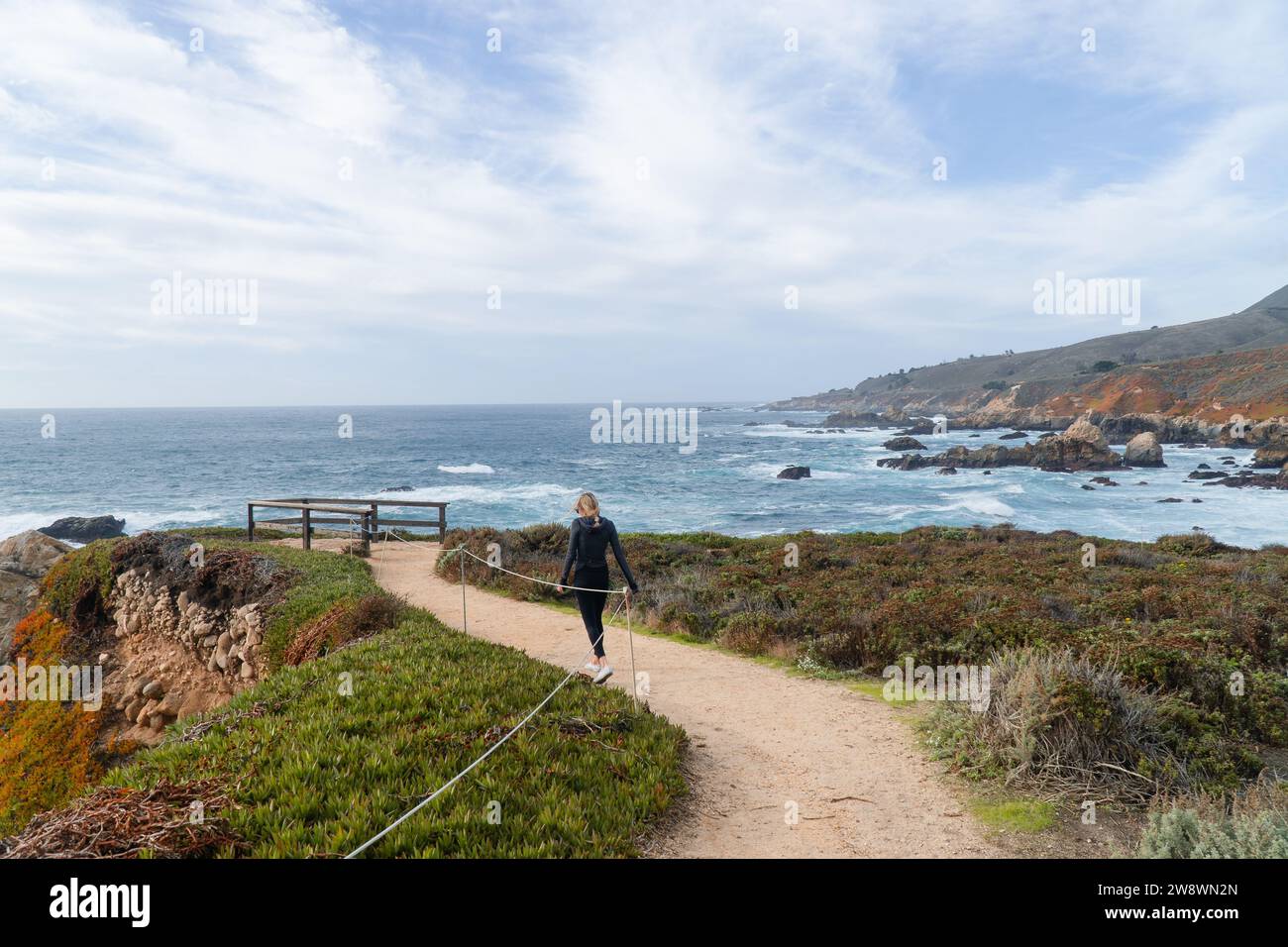 women walking on hiking path along cliff in Big Sur Stock Photo