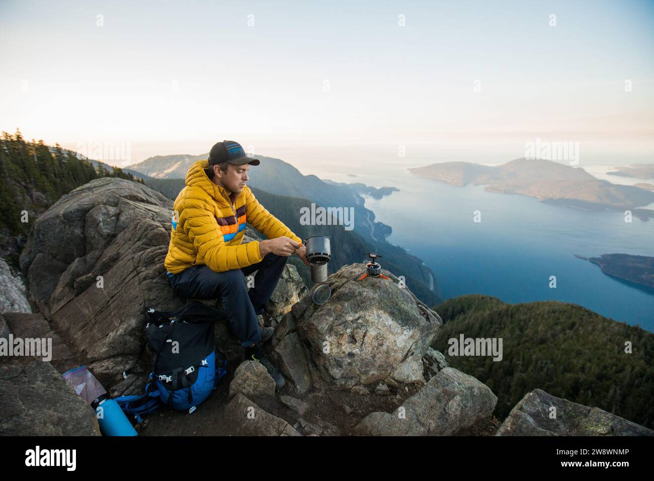 Backpacker using stove on mountain summit with scenic view Stock Photo