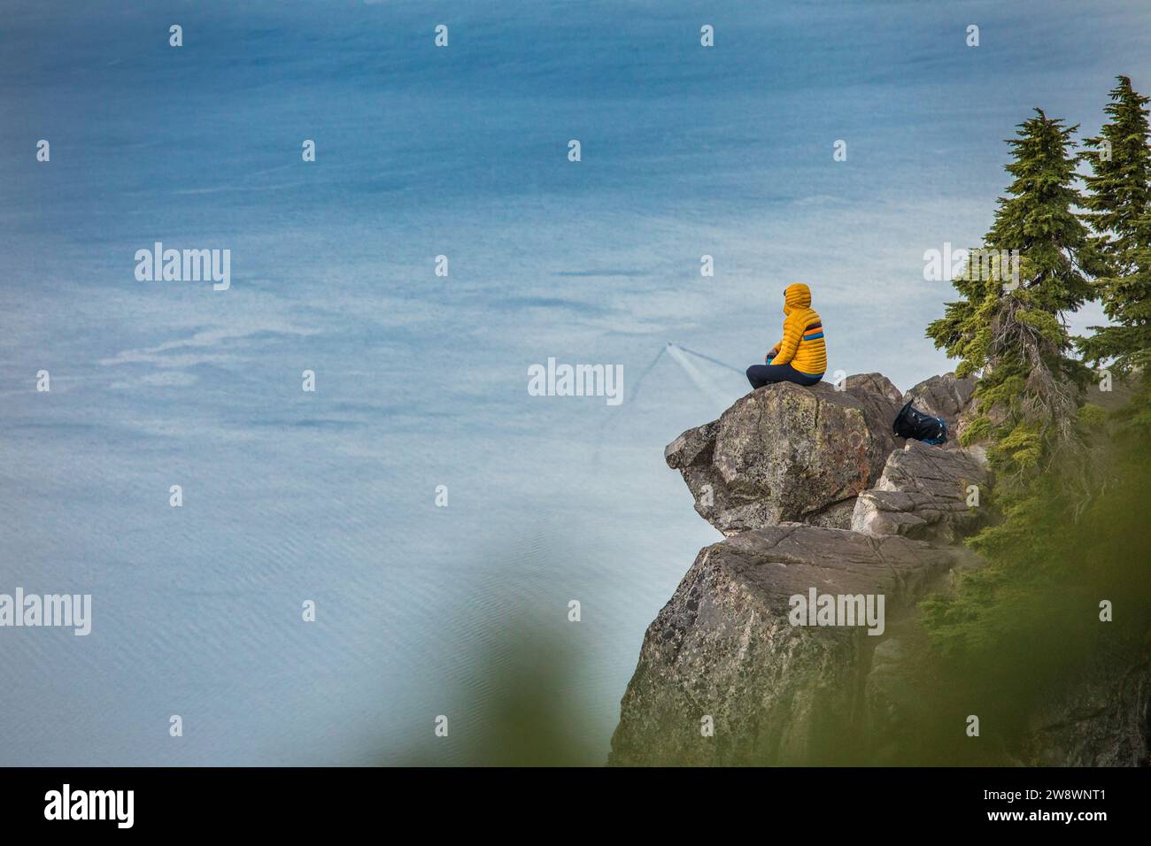 Backpacker sitting on rocky summit enjoying view of Pacific Ocean Stock Photo