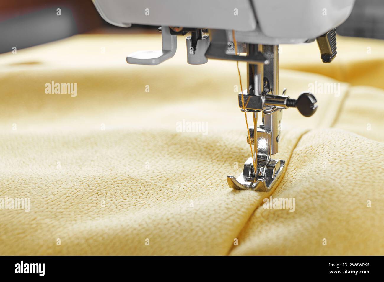 Modern sewing machine with yellow velours fabric. Sewing process clothes, curtains upholstery