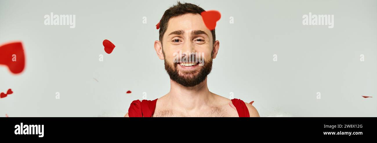 funny cupid man smiling at camera under red heart-shaped confetti, st valentines party, banner Stock Photo