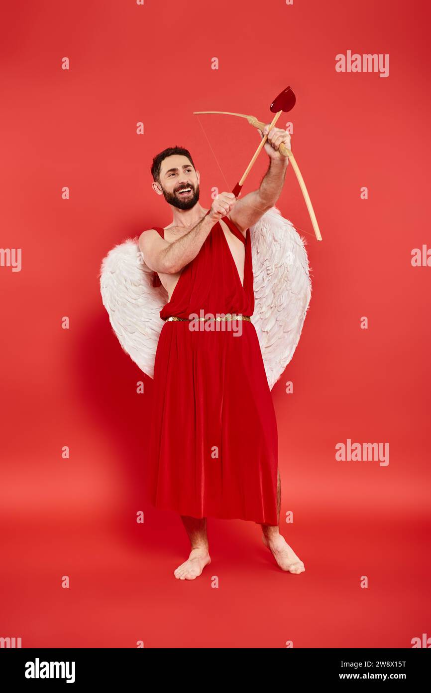 full length of excited man in cupid costume archering on red, Saint Valentines day concept Stock Photo