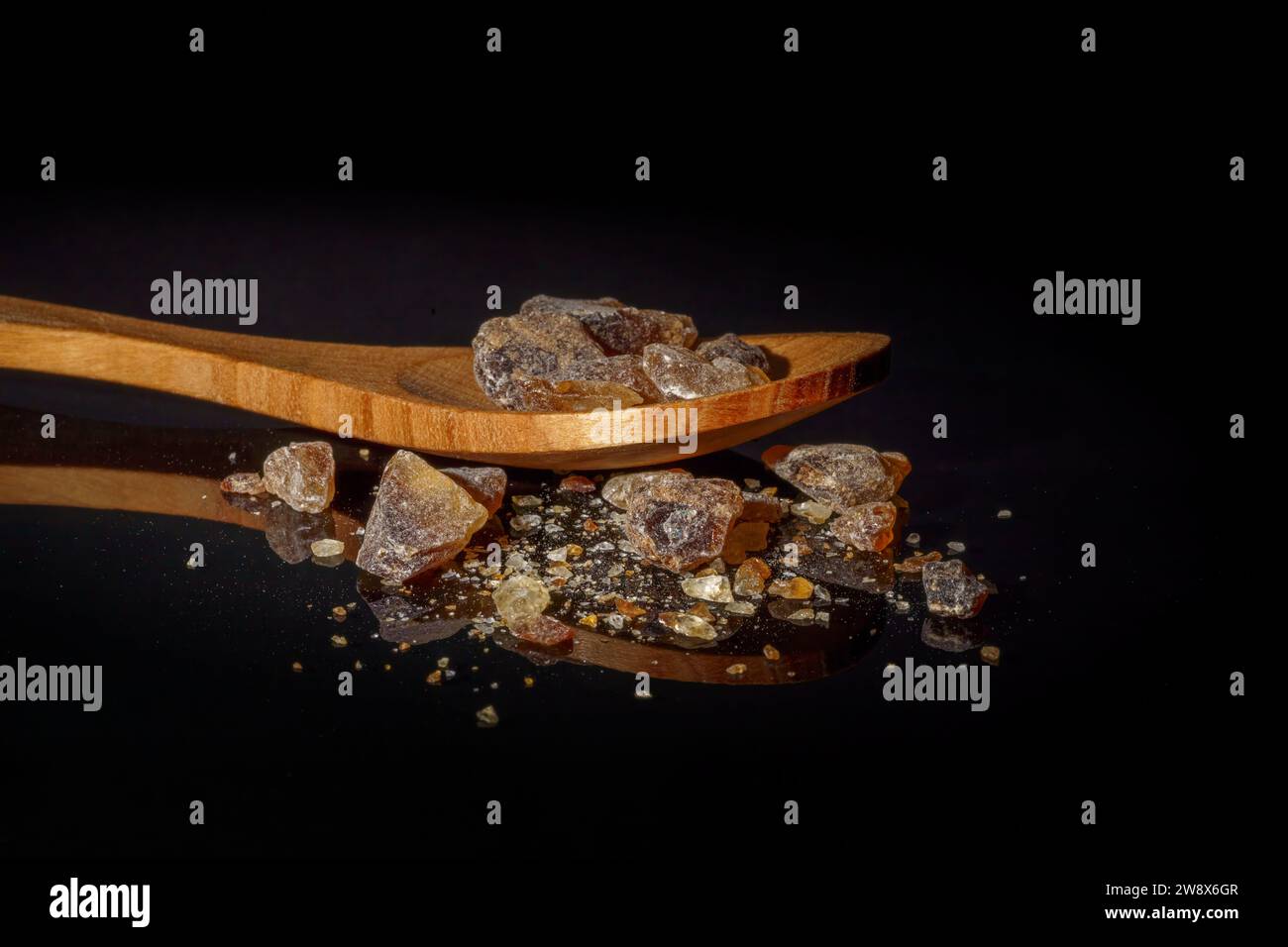 Close-up of brown rock sugar on a wooden spoon with a black background, diabetic concept, with copy space Stock Photo