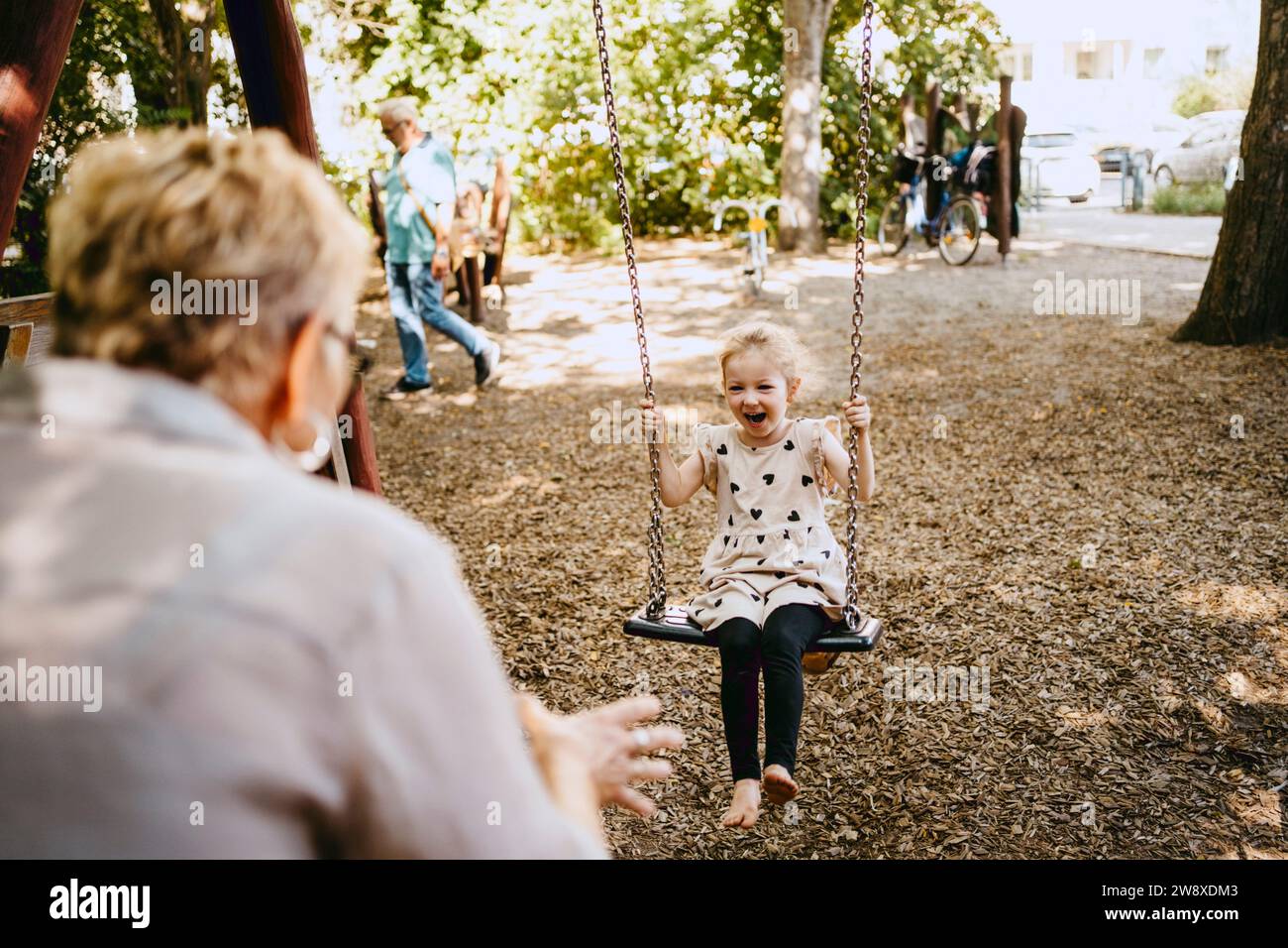 Cheerful girl playing on swing with grandmother at park Stock Photo