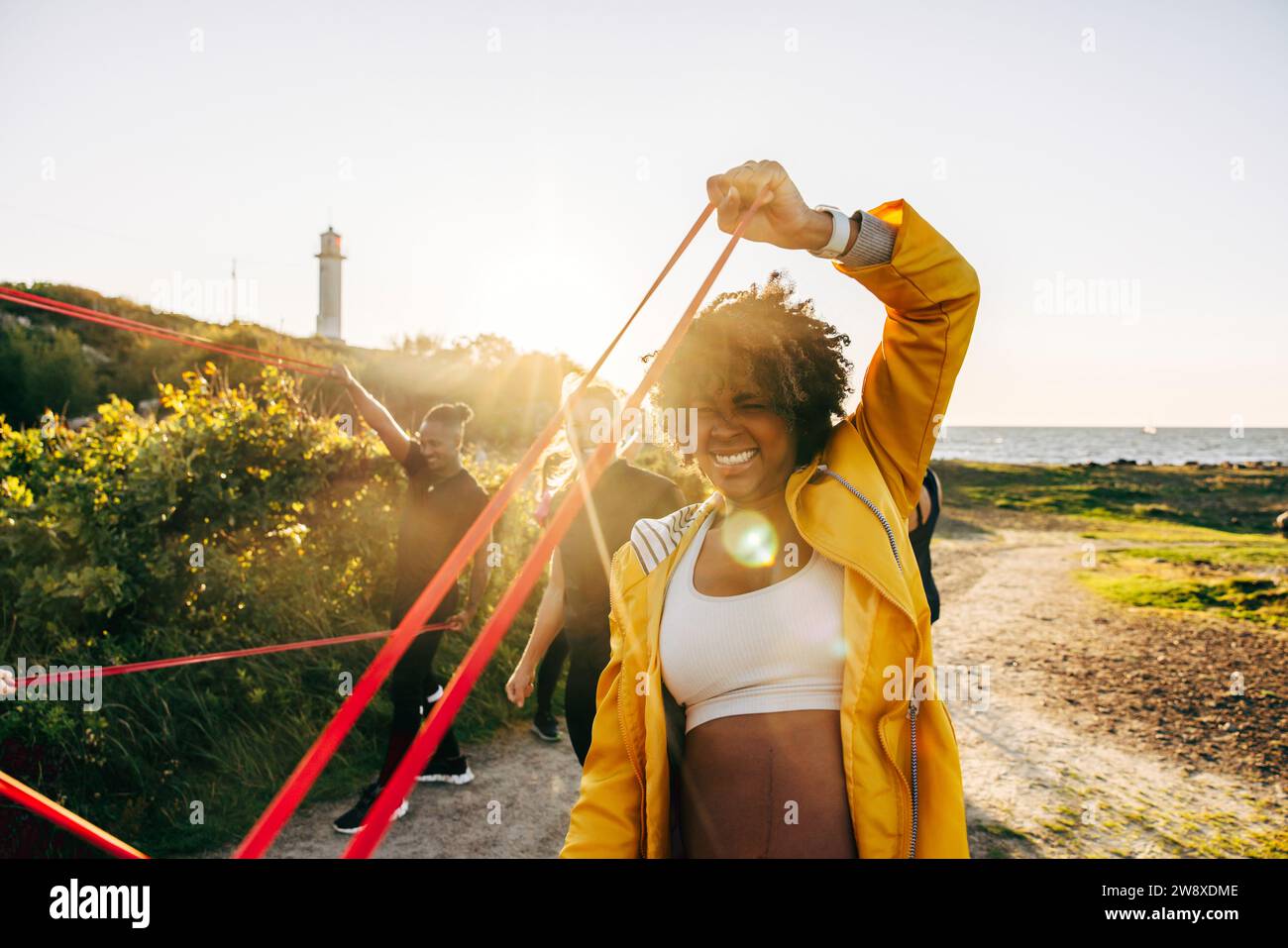Determined woman pulling resistance band during group training at beach ...