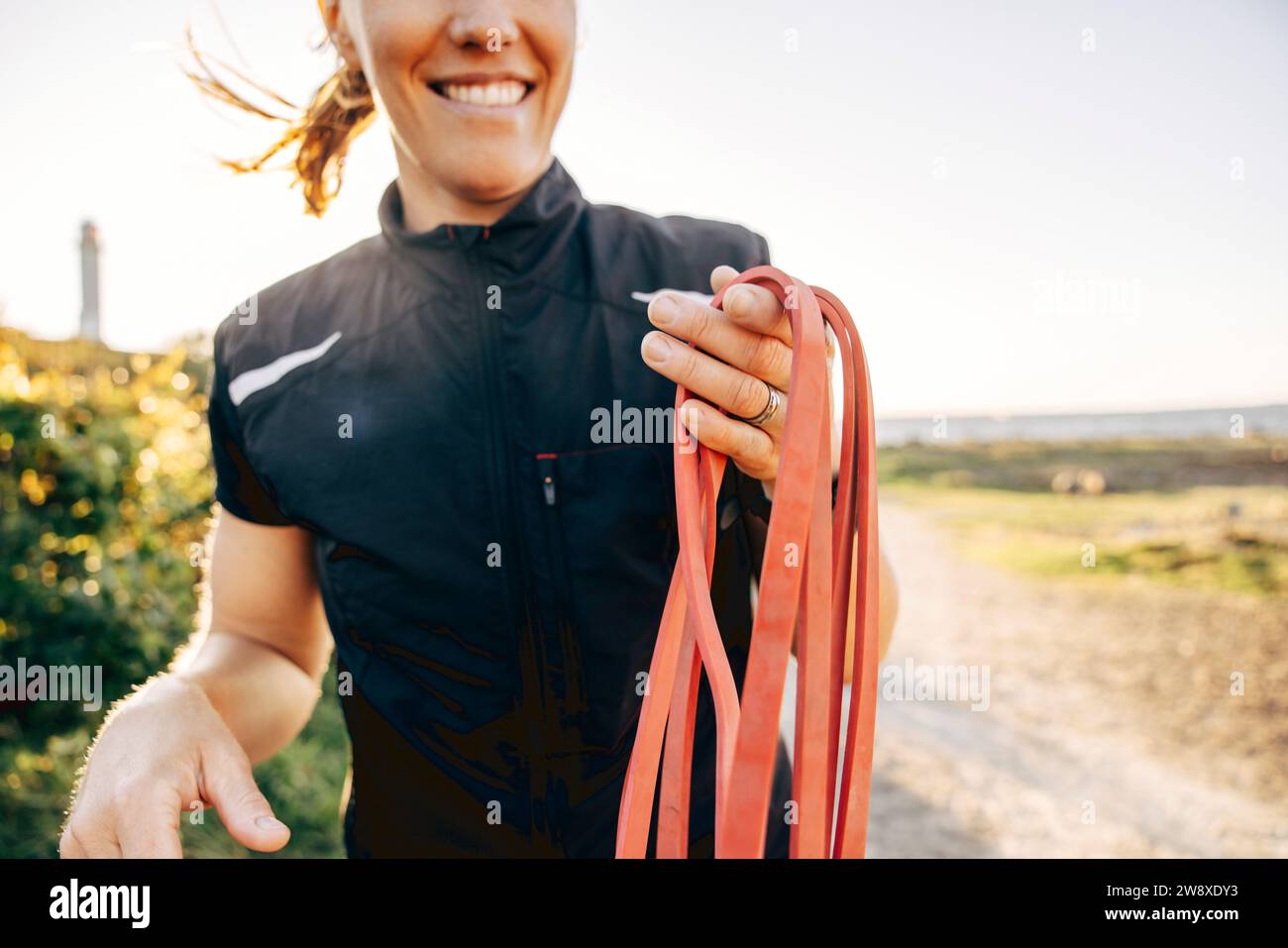 Midsection of smiling female coach holding resistance band at beach Stock Photo