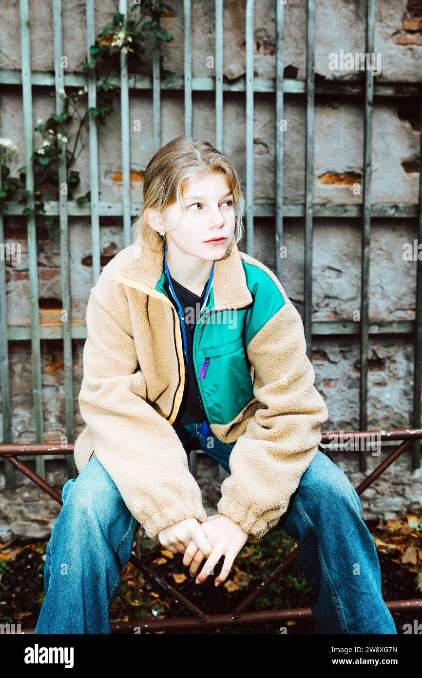 Contemplative girl wearing warm clothing while sitting on railing against wall Stock Photo
