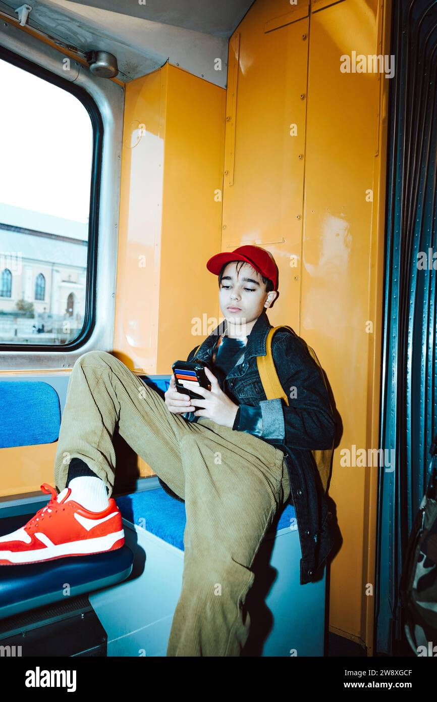 Boy using smart phone while sitting in tram during weekend Stock Photo