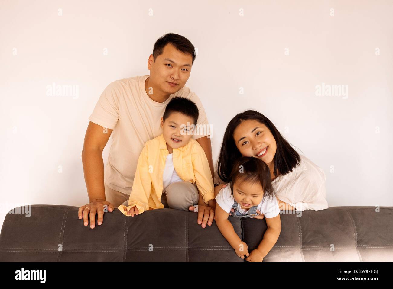 Happy Asian family at home. A Korean couple and their cute little kids on the sofa in the living room. Parents and their son and daughter pose togethe Stock Photo