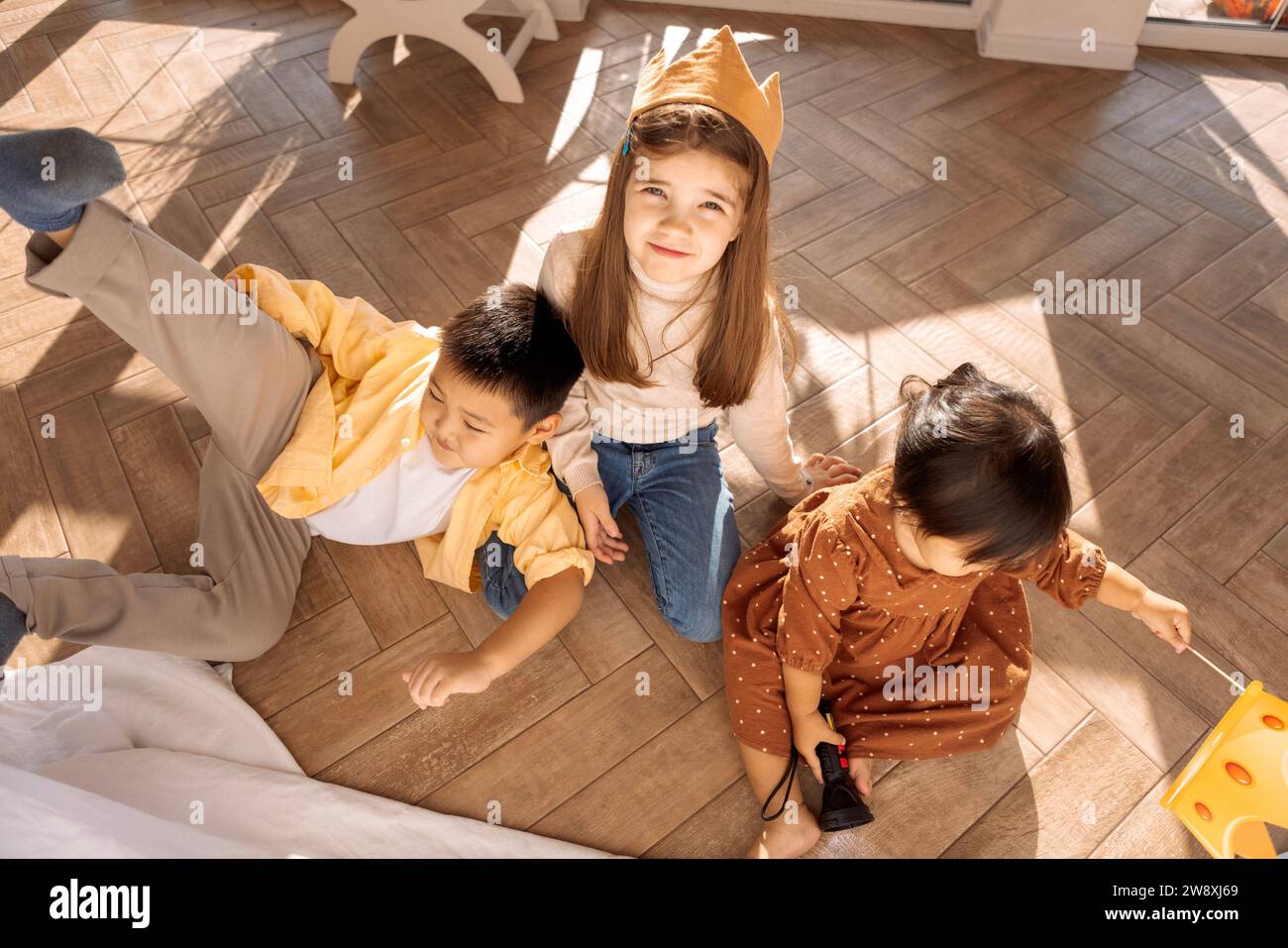 Cute children of different races play together. Asian sibling and caucasian girl are messing around in the bedroom on the floor. Small children have f Stock Photo