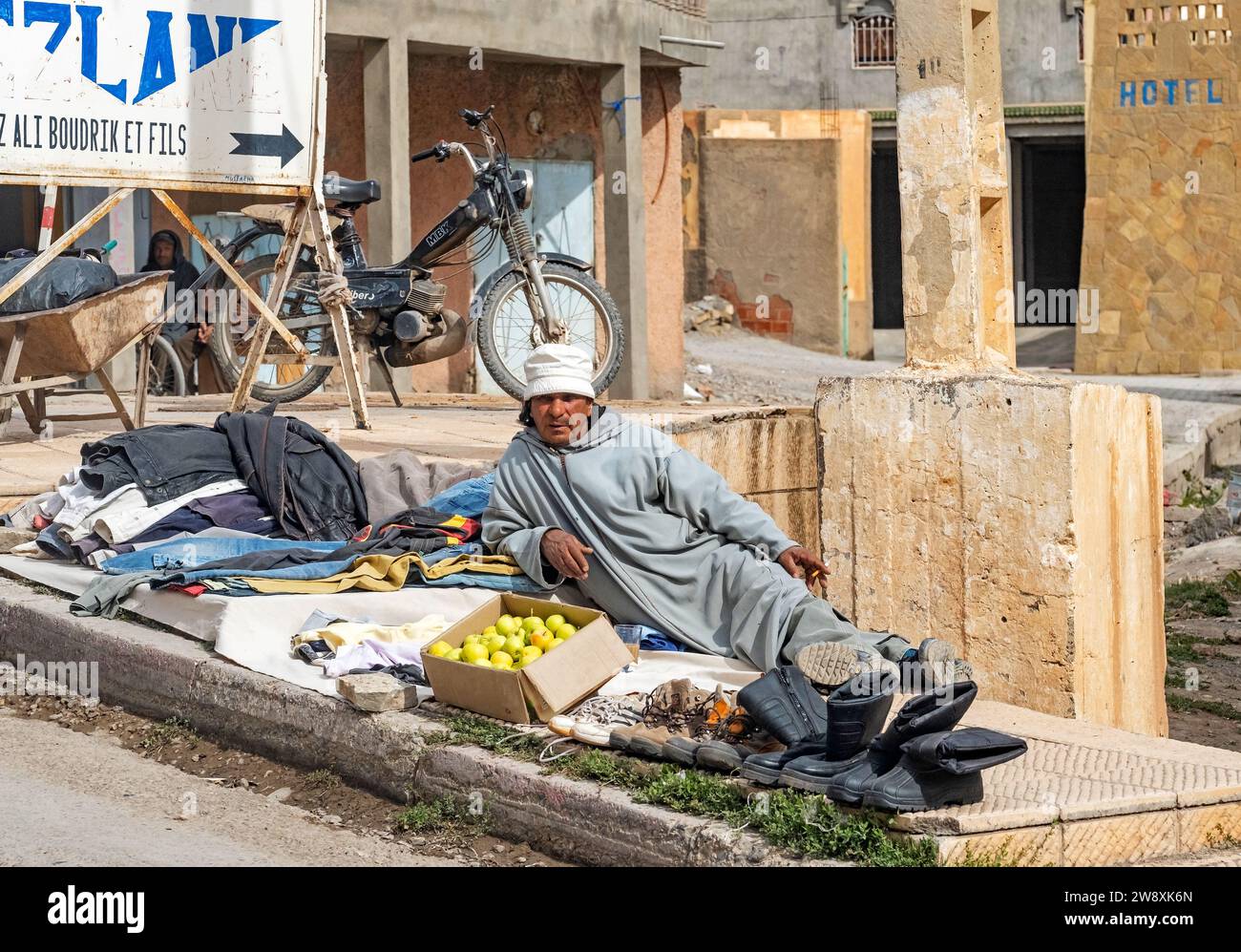 Moroccan street vendor selling clothes, shoes and apples in village Imilchil / Imilshil, High Atlas Mountains, Midelt Province, Morocco Stock Photo