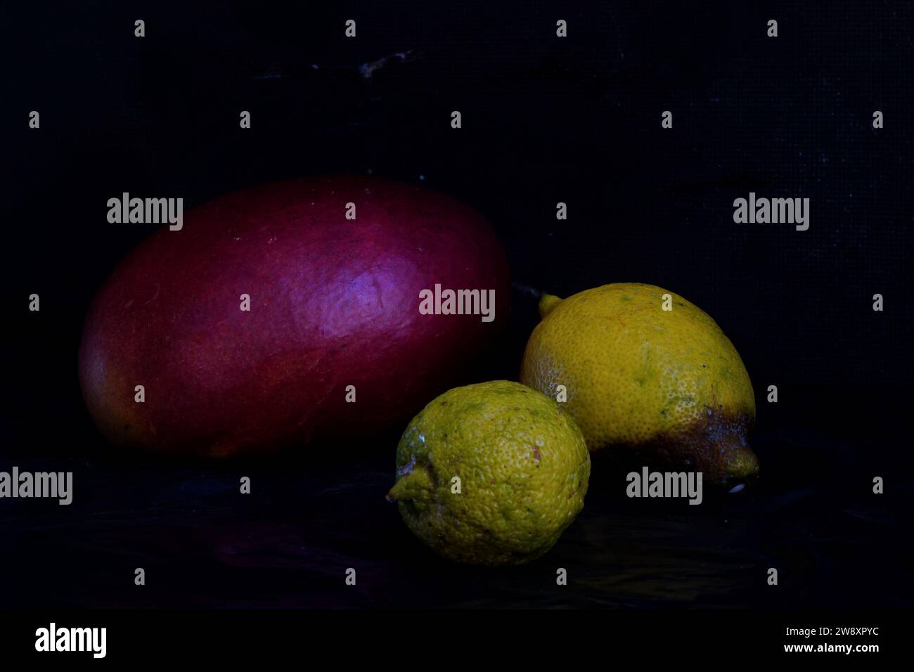 Still life with red mango, yellow lemons and dark background Stock Photo