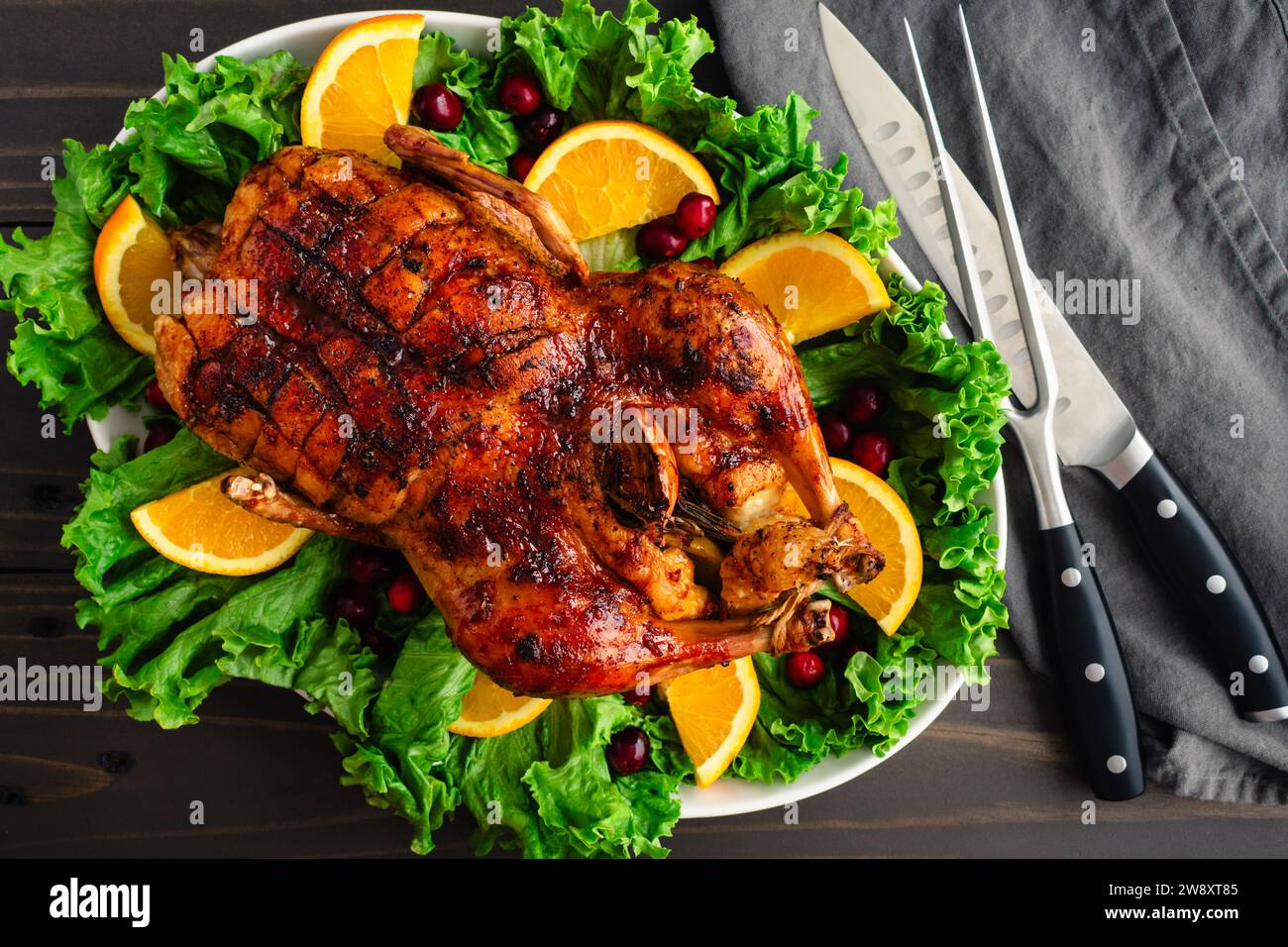 Christmas Roast Duck With Cranberry-Orange Glaze: Roasted and glazed whole duck on a garnished platter with carving knife and fork Stock Photo