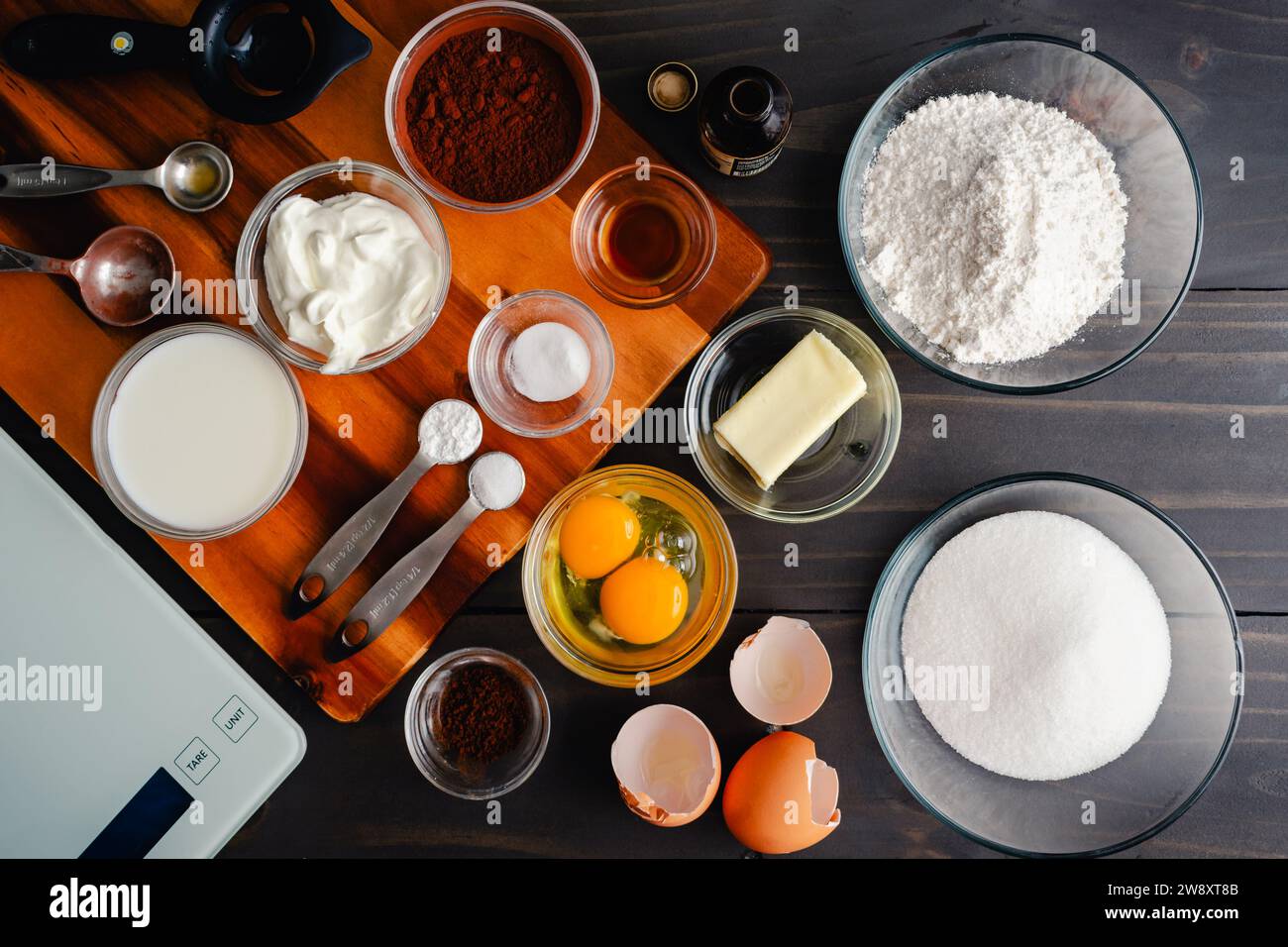 Measured and Weighed Chocolate Cake Ingredients: Overhead view of cake ingredients in prep bowls with measuring spoons, egg separator, and scale Stock Photo