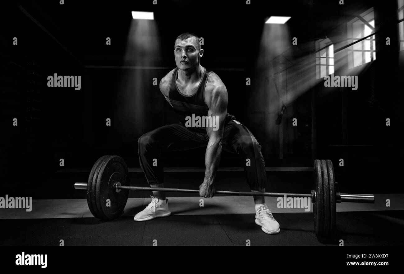 Athlete is standing on his knee and near the bar and is preparing to make a deadlift. Mixed media Stock Photo