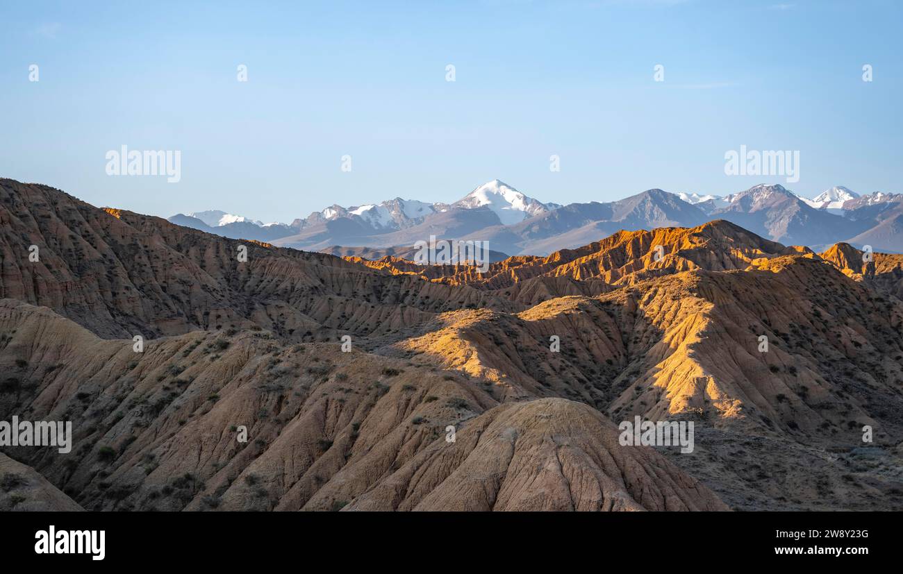 Tianshan Mountains Rivers Landscape of eroded hills at sunrise, badlands, white mountain peaks of ...