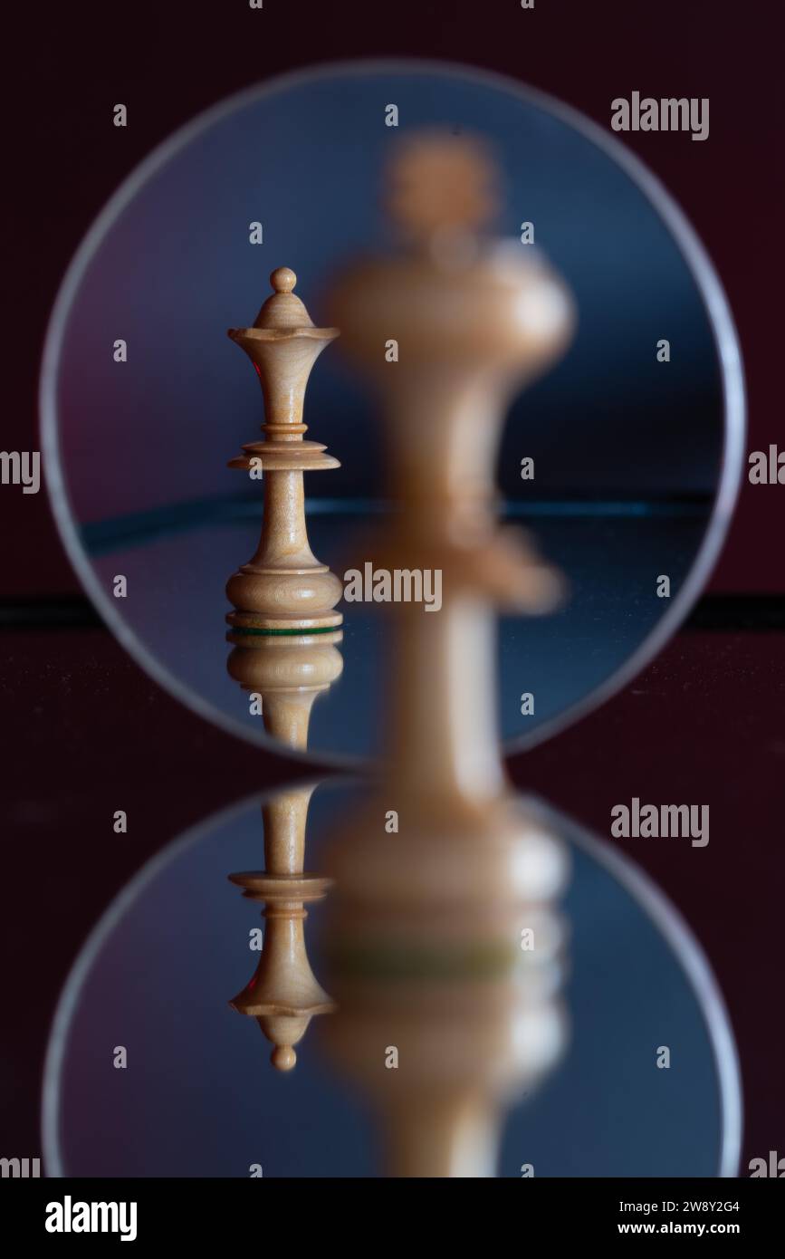 A queen chess piece can be seen in a mirror, in front of it stands a king on a reflecting background, chess game, symbolising power, relationship Stock Photo