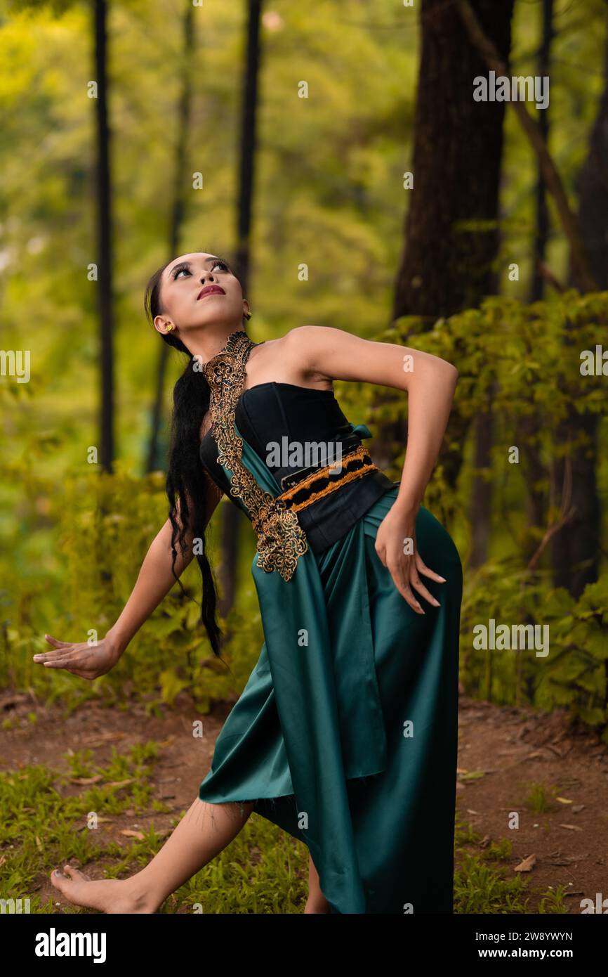 Beautiful Asian woman in a green costume with long black hair dances in ...